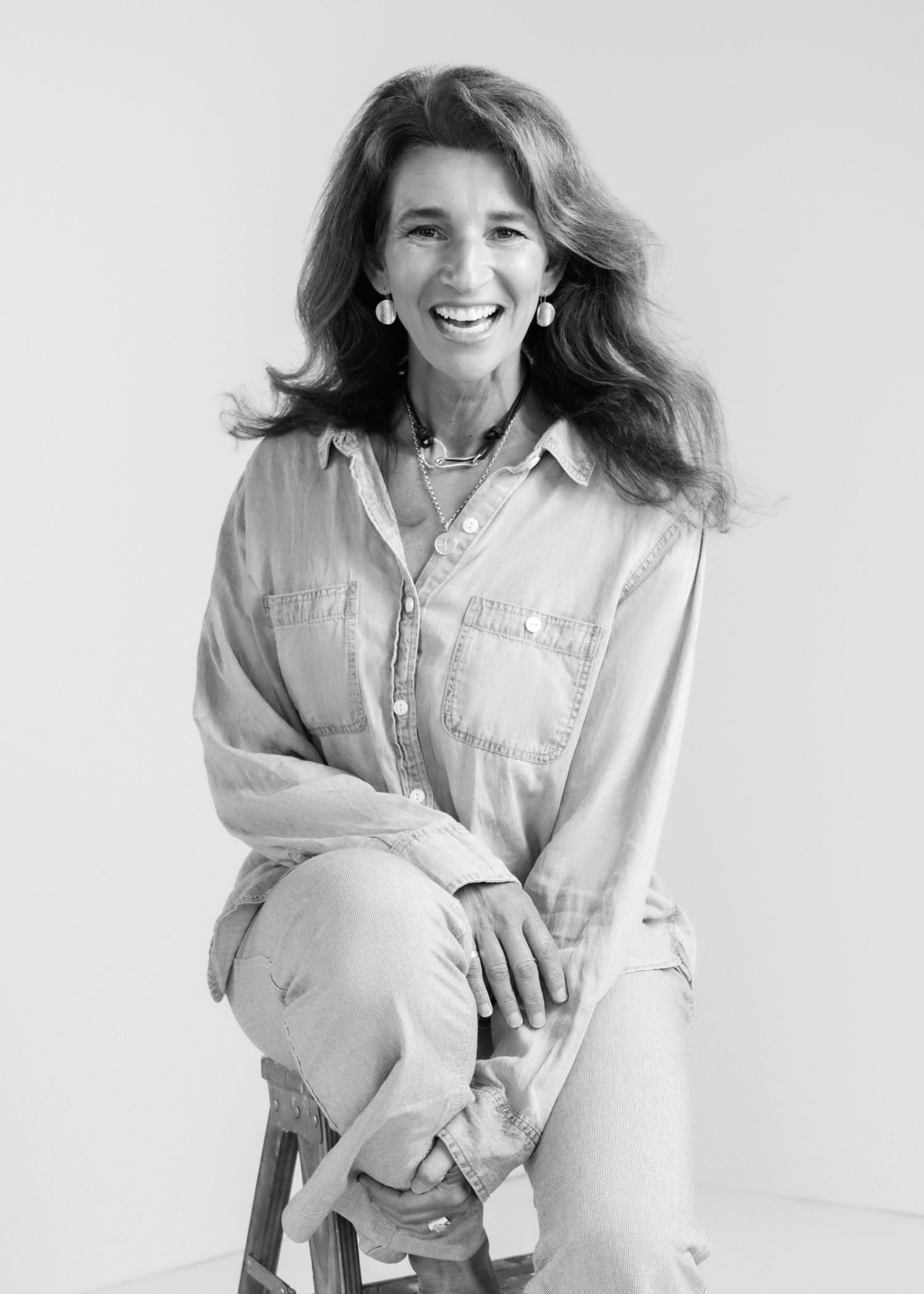 Professional portrait of a woman in casual denim shirt sitting and smiling against white background.