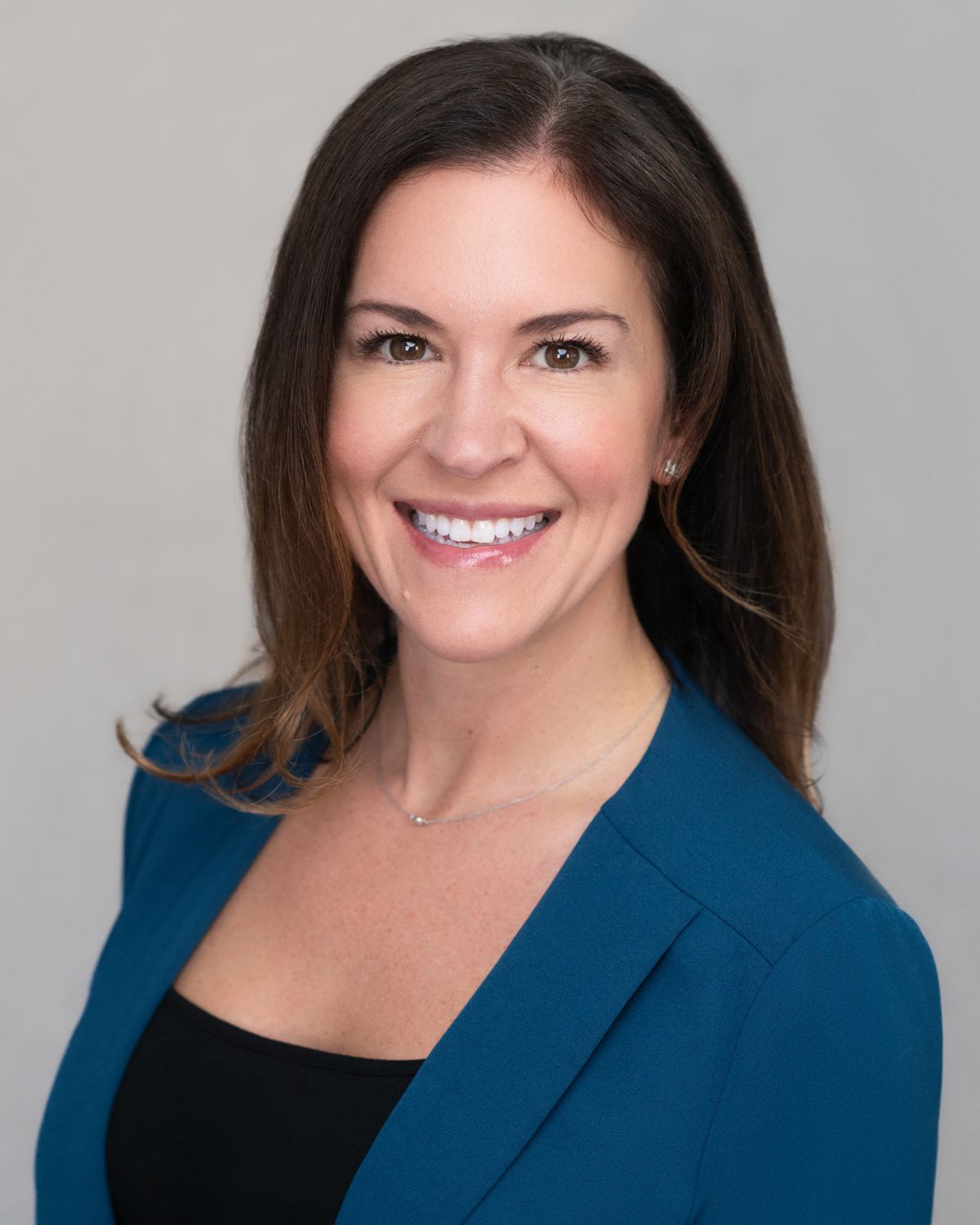 Professional portrait of person in blue blazer and black top against gray background.