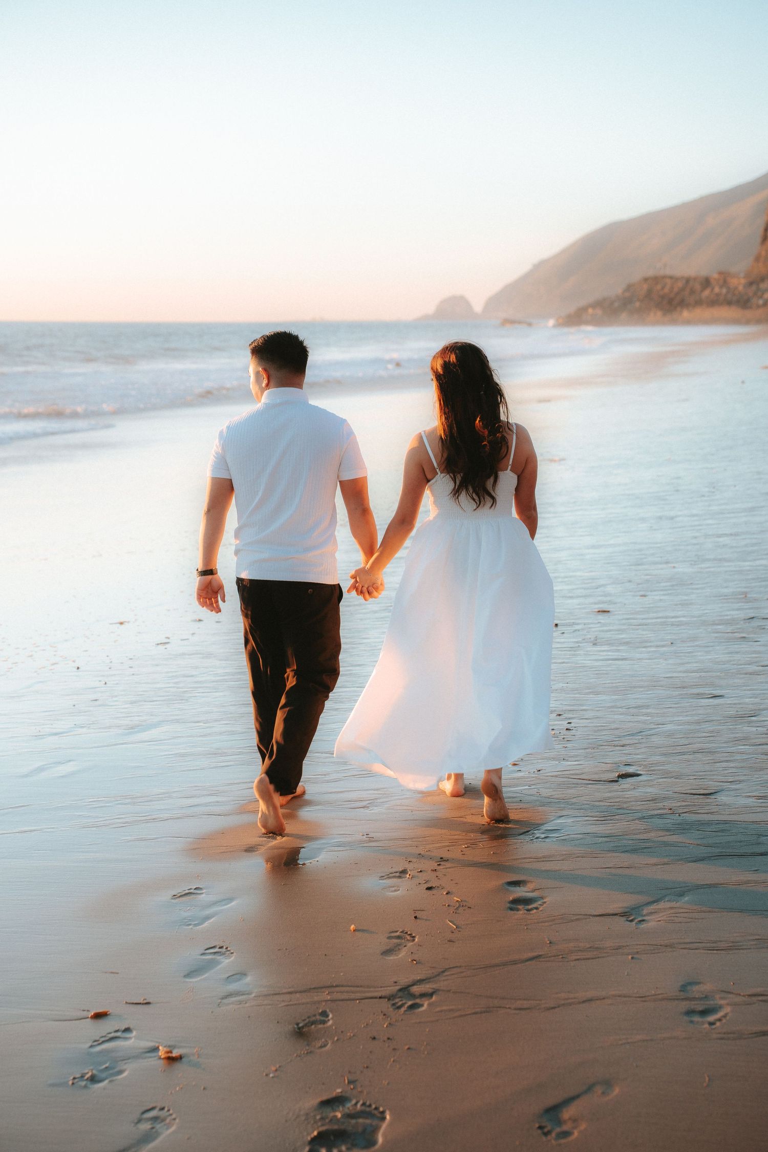 Couple walking together on a scenic beach at sunset leaving footprints in the sand.