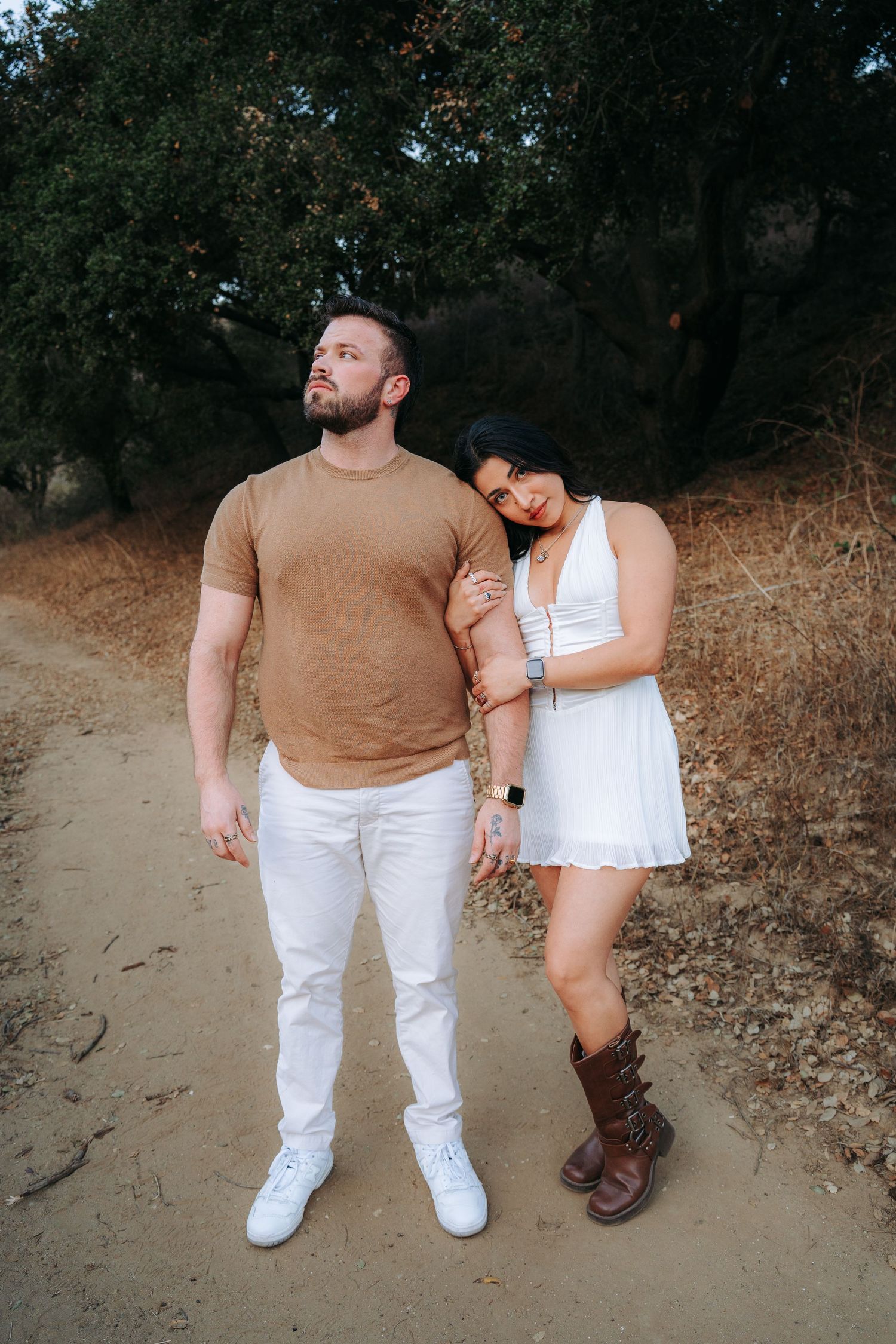 Couple walking together on a dirt trail surrounded by dry brush and trees.