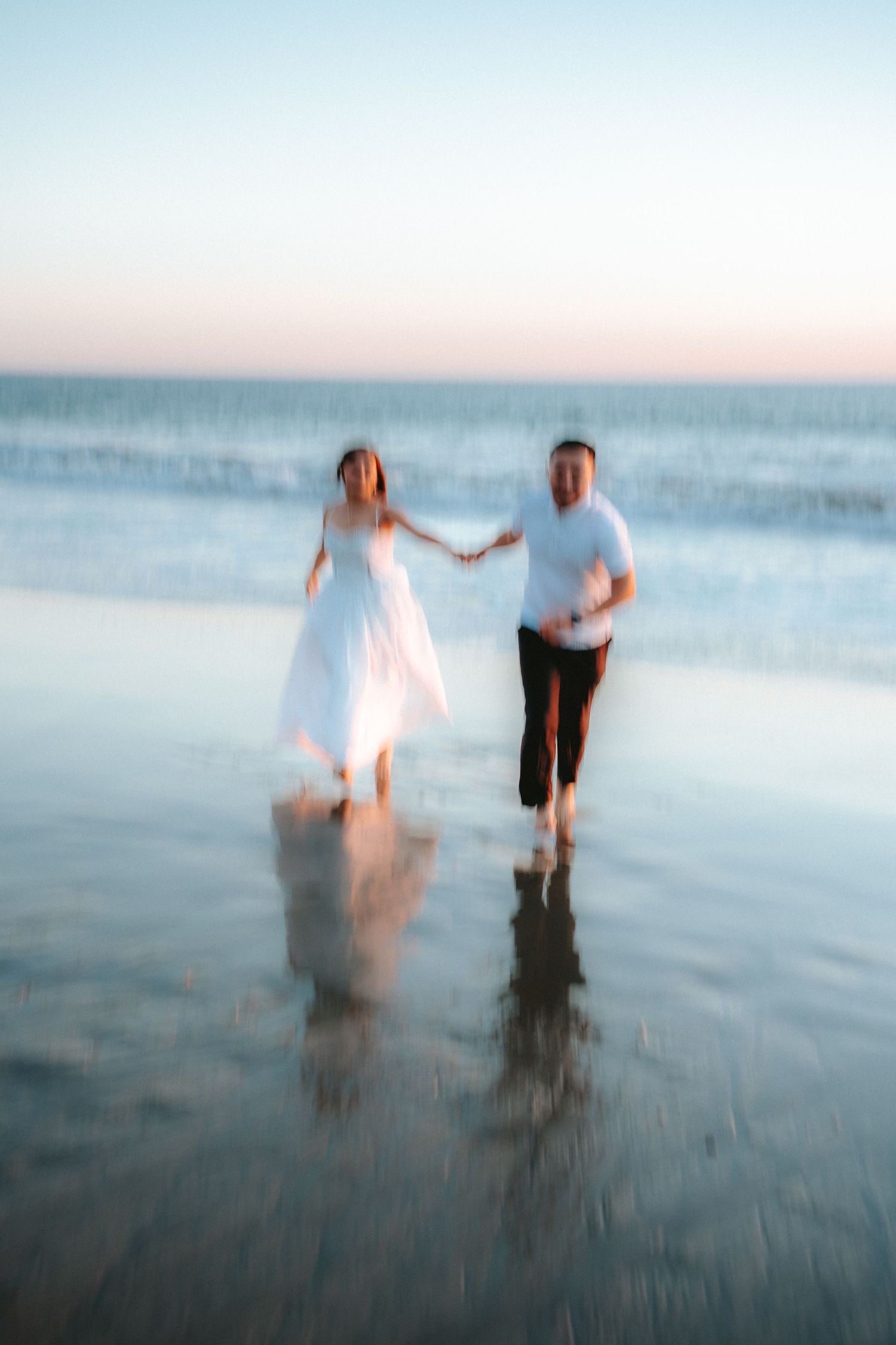 Dreamy motion blur photo of couple walking in ocean waves at dusk.