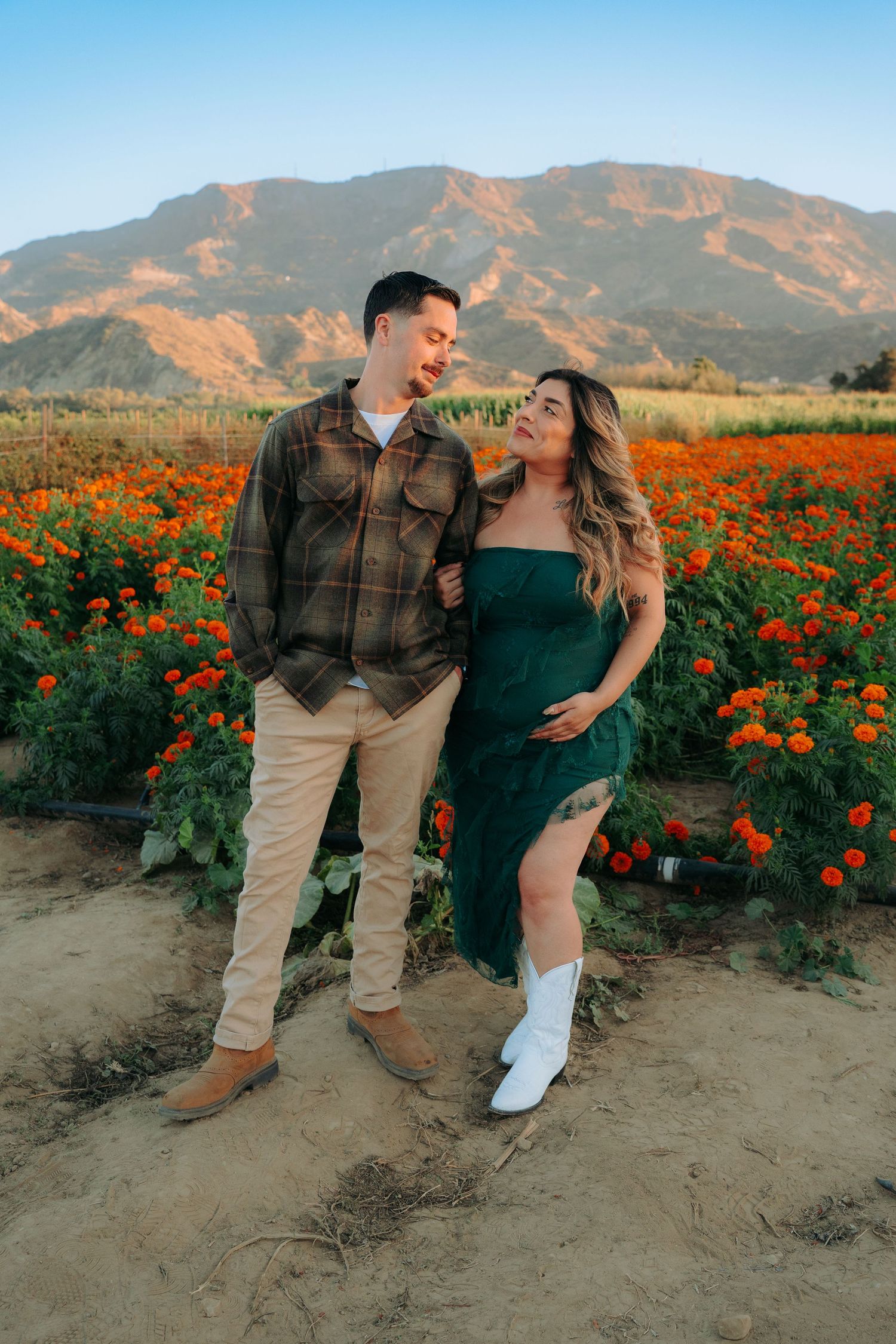 Romantic couple posing playfully in a vibrant orange flower field with mountains in the background.