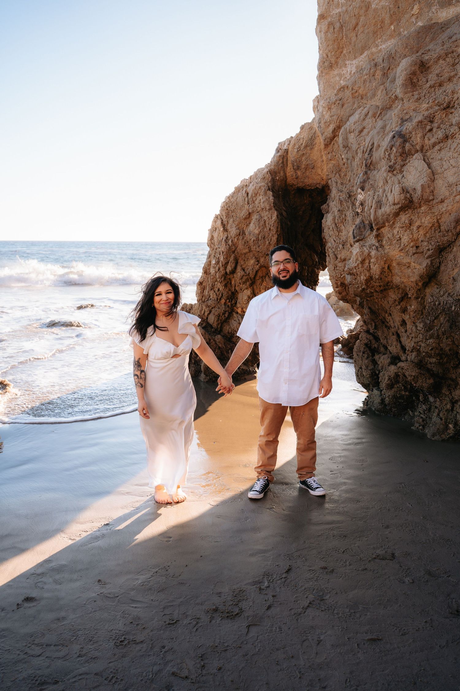 Couple holding hands on Malibu Beach, captured in a cinematic, in-the-moment engagement session with timeless elegance.