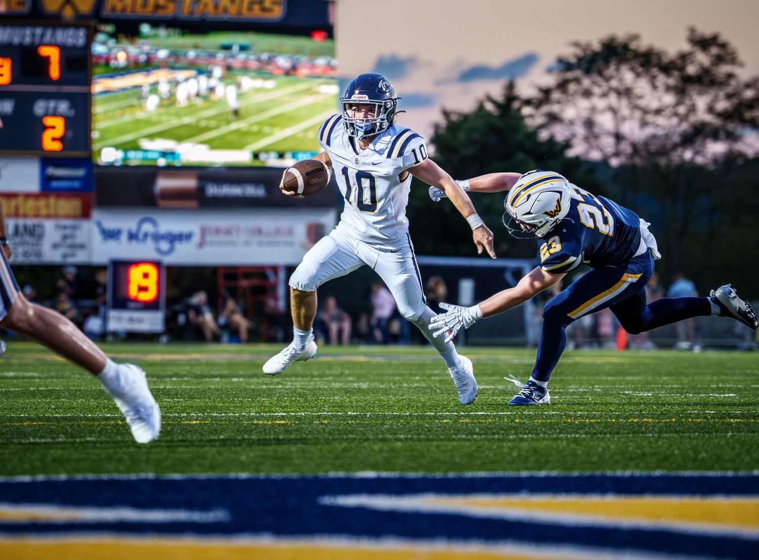 Football players diving to make plays on a grass field at sunset.