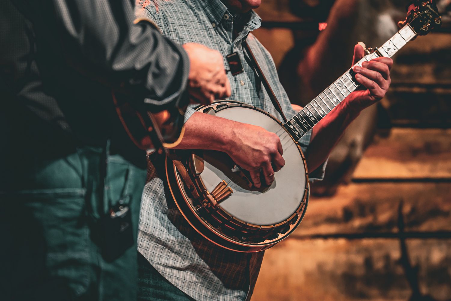 Close-up of musicians playing banjo and guitar at a bluegrass jam session with rustic wooden background.