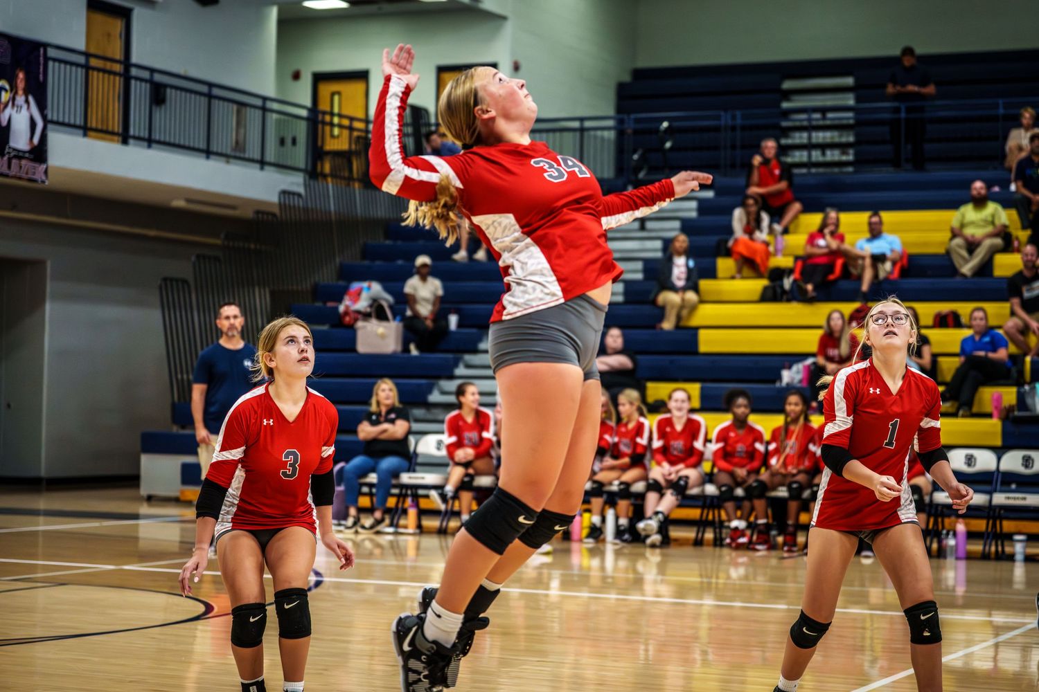 Volleyball players in red uniforms jumping and diving during an intense match.