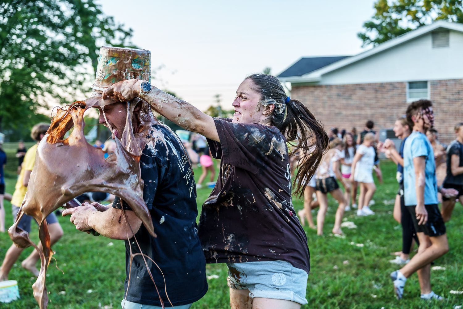 Students engage in a messy outdoor food fight activity on a green lawn during a school event.