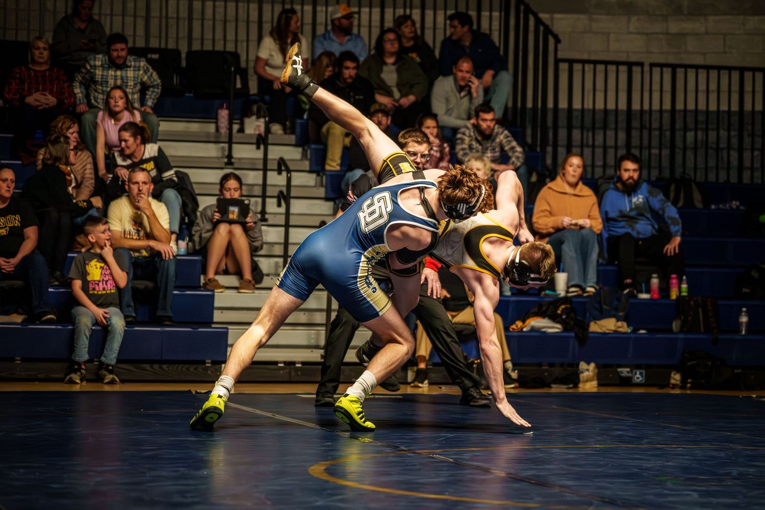 High school wrestlers compete in a match on a blue mat during an indoor tournament.