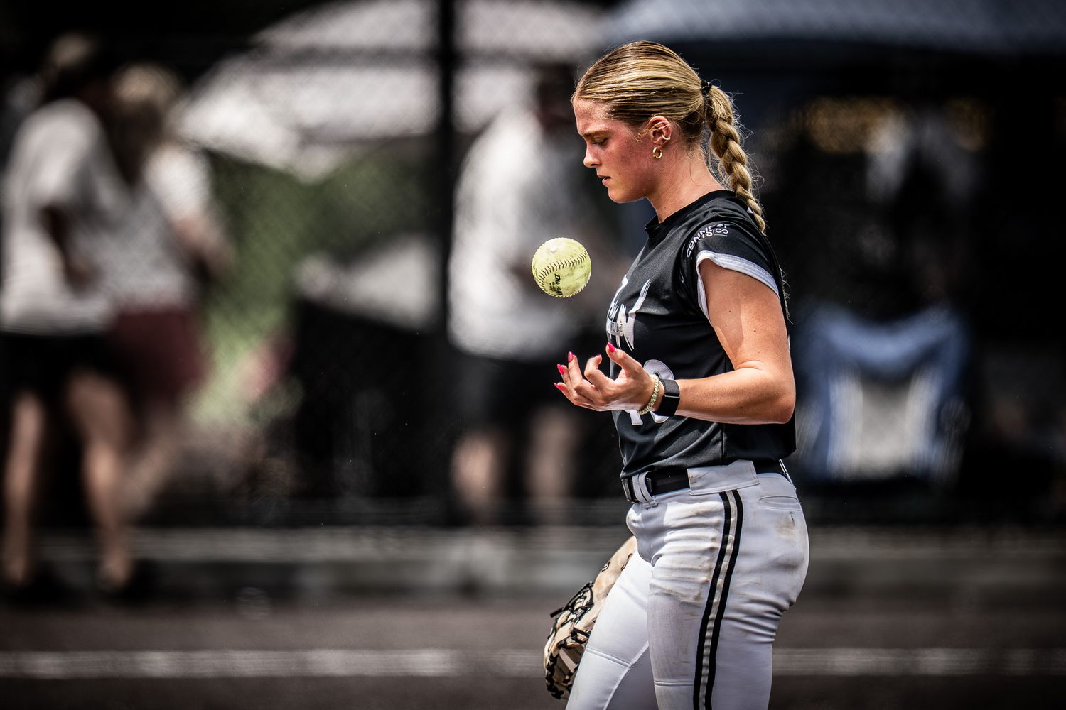 Female softball player in black uniform tossing a yellow ball on the field during a competitive game.
