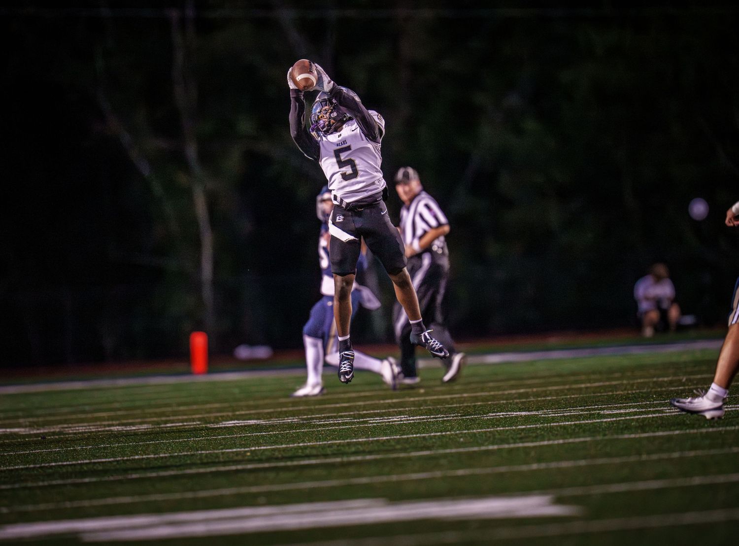 Football players in action during a night game on an illuminated field.