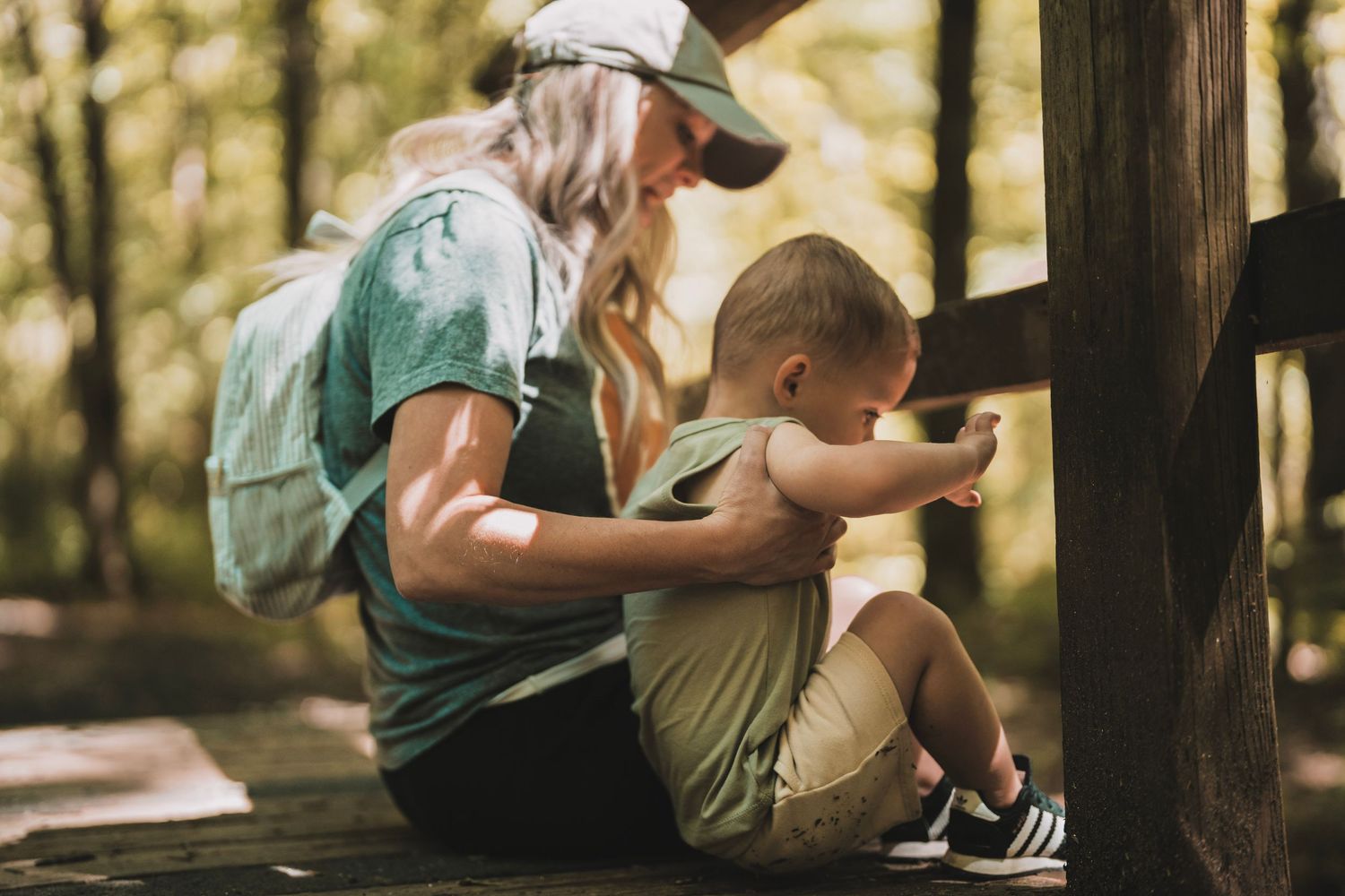 Two people sitting together on wooden steps in a forest setting with backpack and casual outdoor attire.