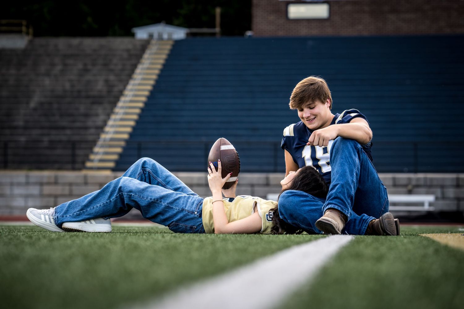 Athletes resting on a football field with stadium seating in the background.