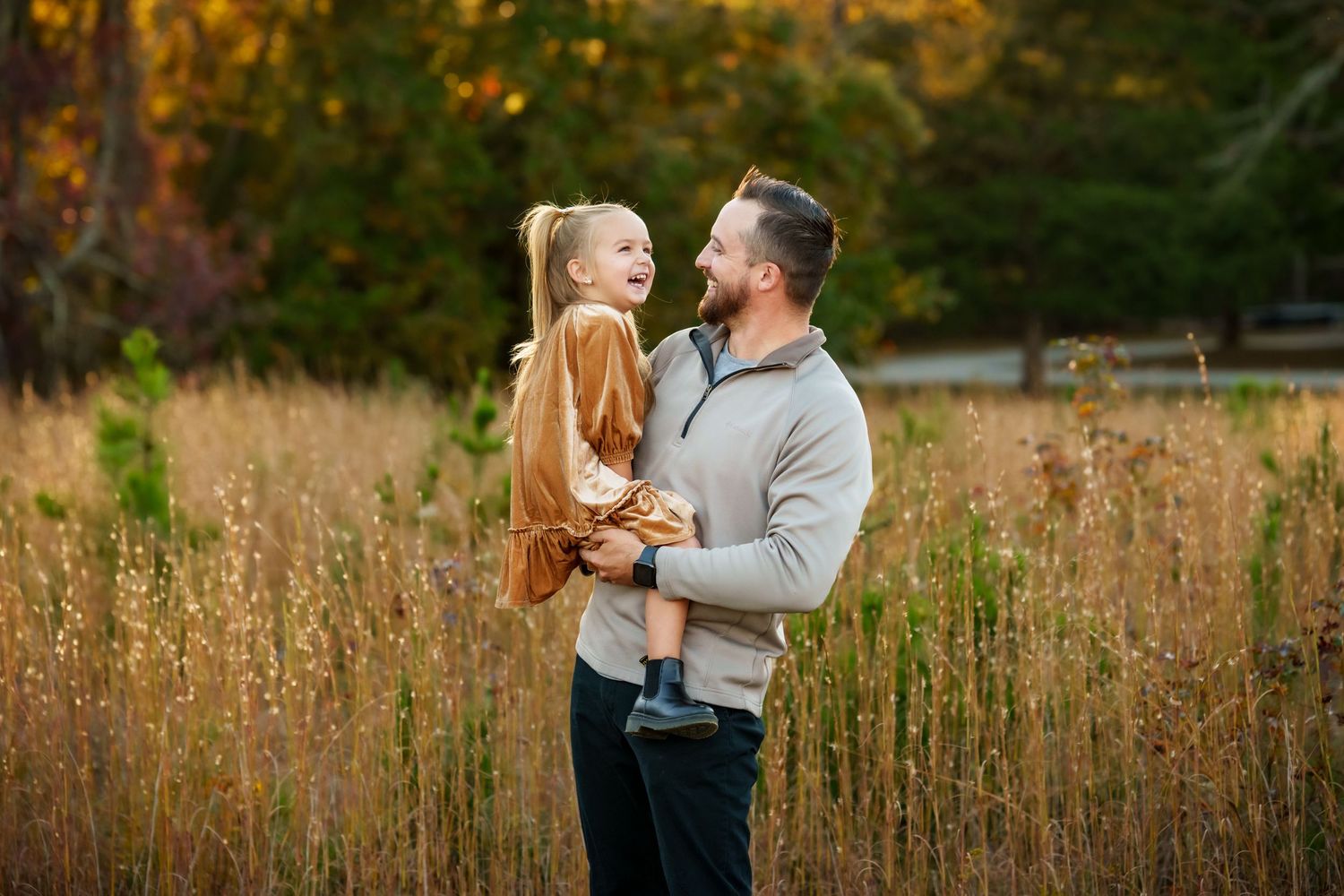 A loving moment captured in a golden autumn field with tall grass and warm sunset lighting in the background.
