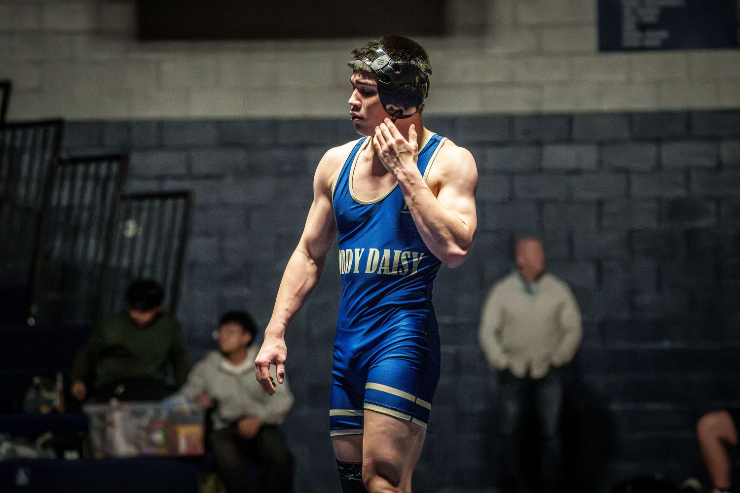 Wrestler in blue singlet competes during an intense match on a wrestling mat.