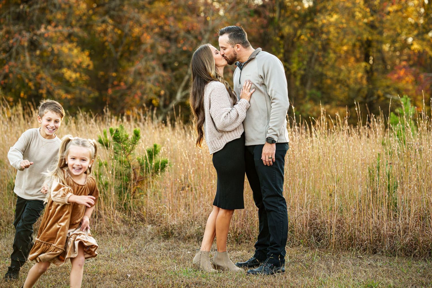 Romantic couple embraces in golden autumn field during sunset photoshoot.