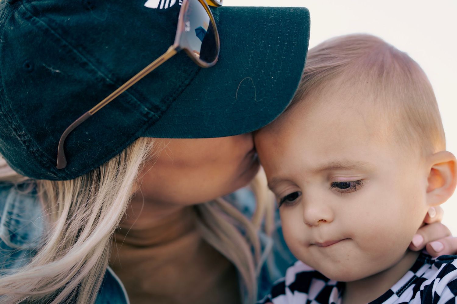 A tender moment captured between a parent wearing a green baseball cap and a young child in close-up.