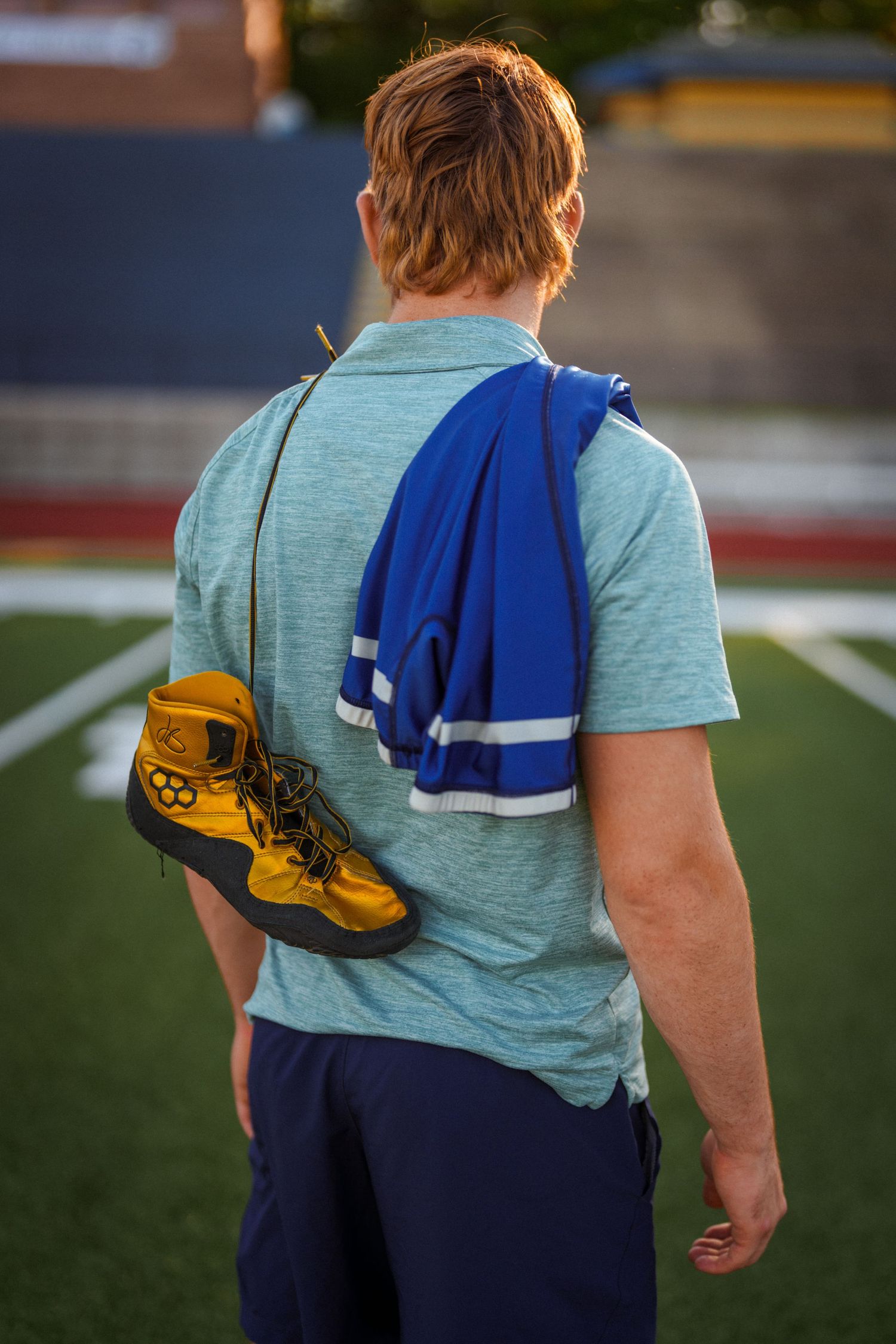 Athlete carrying sports equipment with blue towel walking on field.