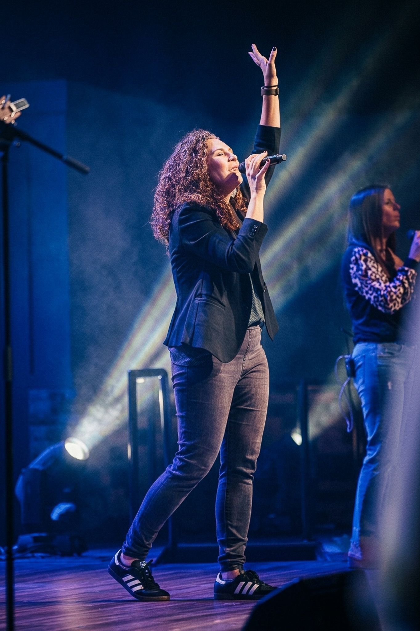 A female singer performs on stage with one arm raised, holding a microphone under blue stage lights.