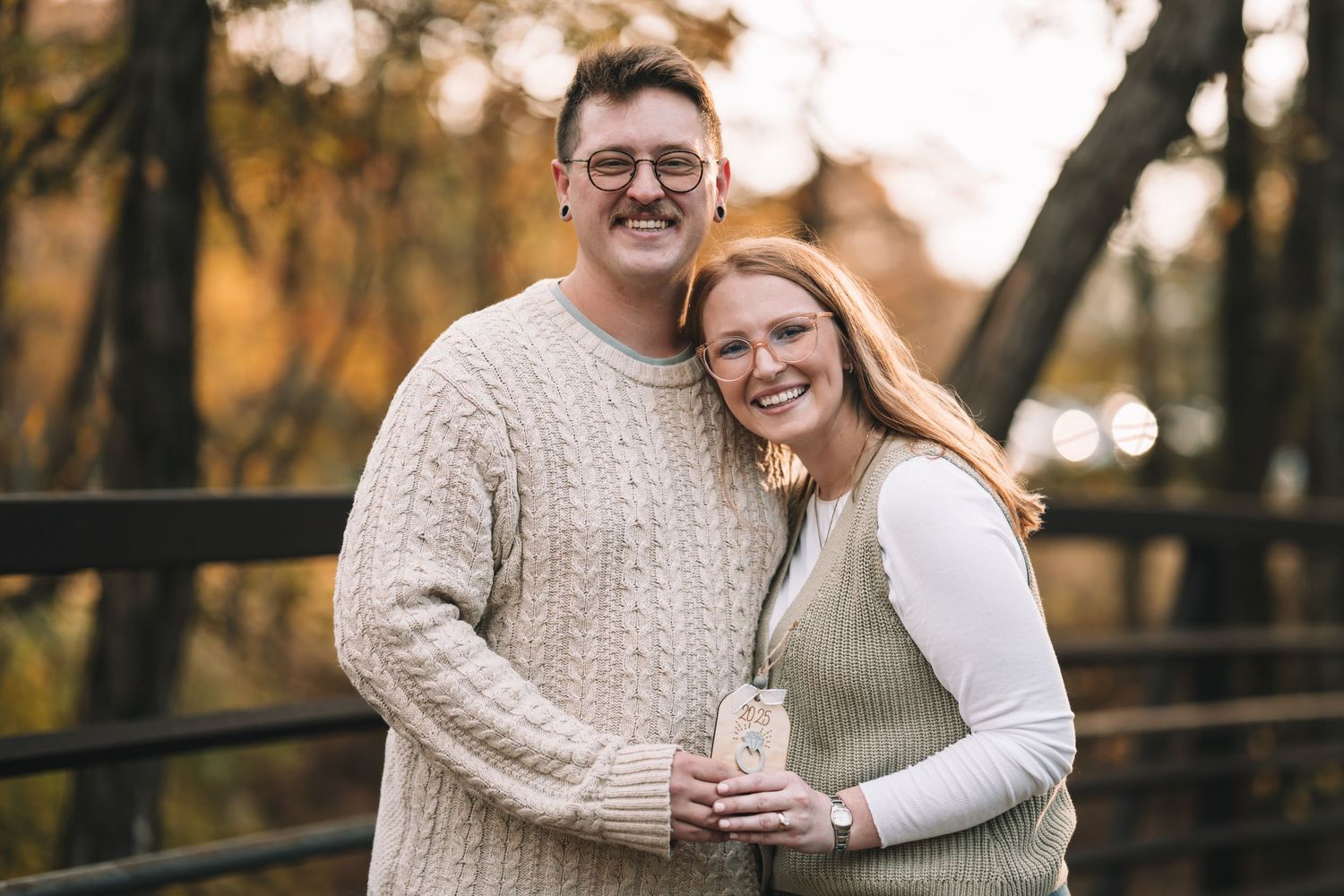 A couple wearing cozy sweaters embraces and laughs together during an autumn outdoor photoshoot.