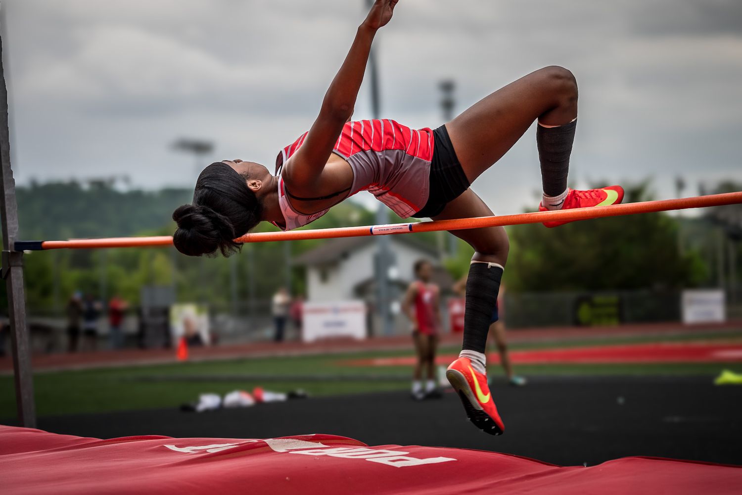 Athletes performing high jump attempts over a red bar at a track and field competition.