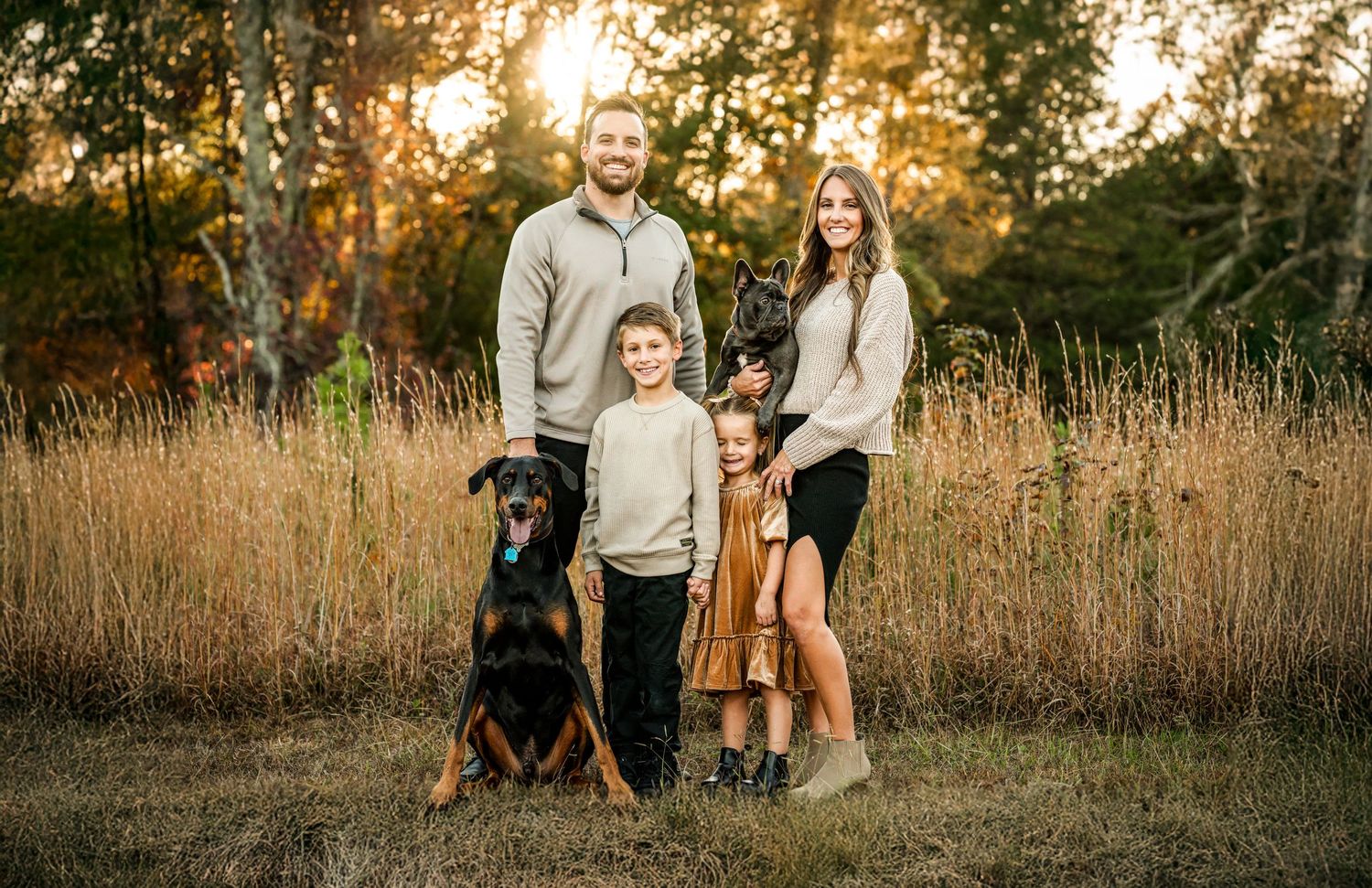 A group in coordinating beige and brown outfits poses together at sunset in a golden field of tall grass.