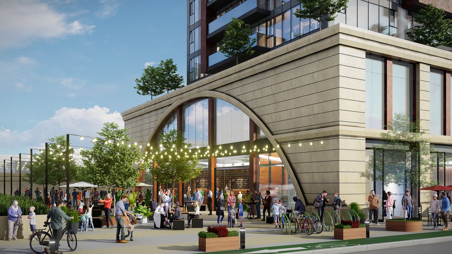 Modern urban development with glass buildings, pedestrian walkways and outdoor seating areas under blue skies.