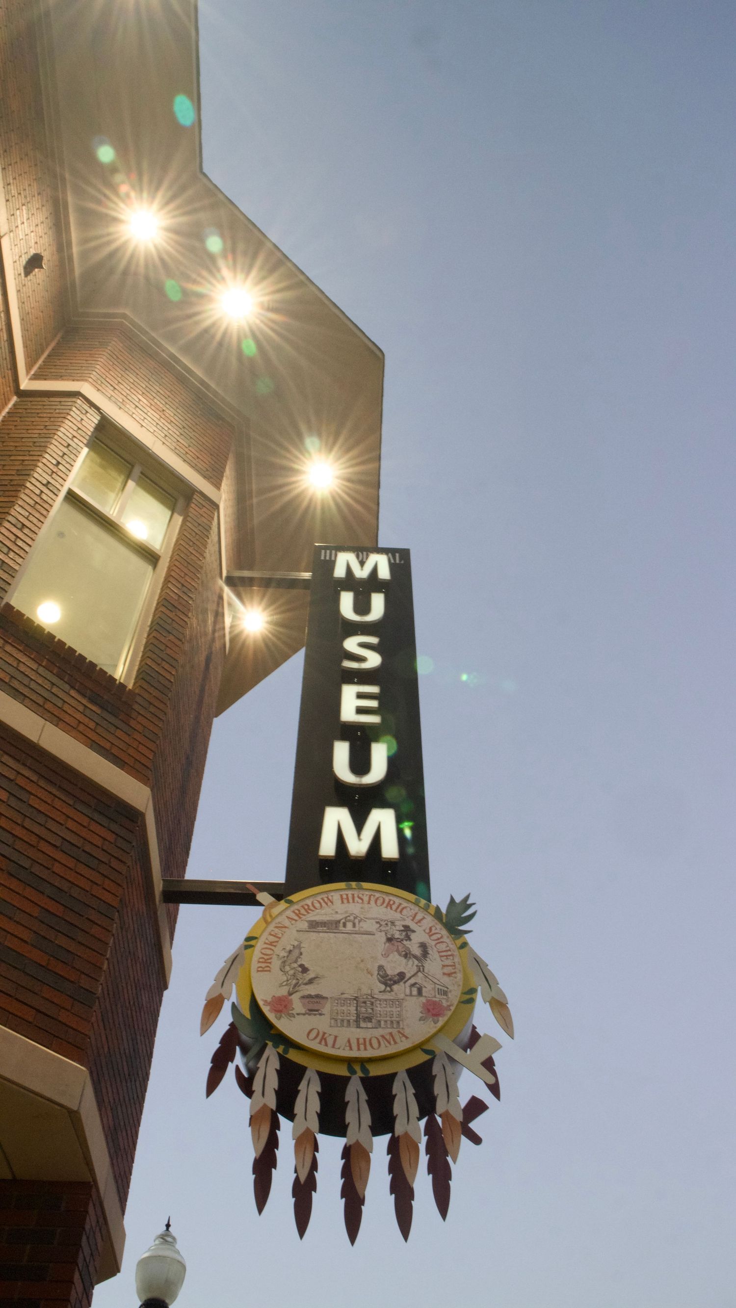 Low-angle shot of The Museum Broken Arrow sign with sunflare, showcasing professional architectural photography by Haug & Bees Media.