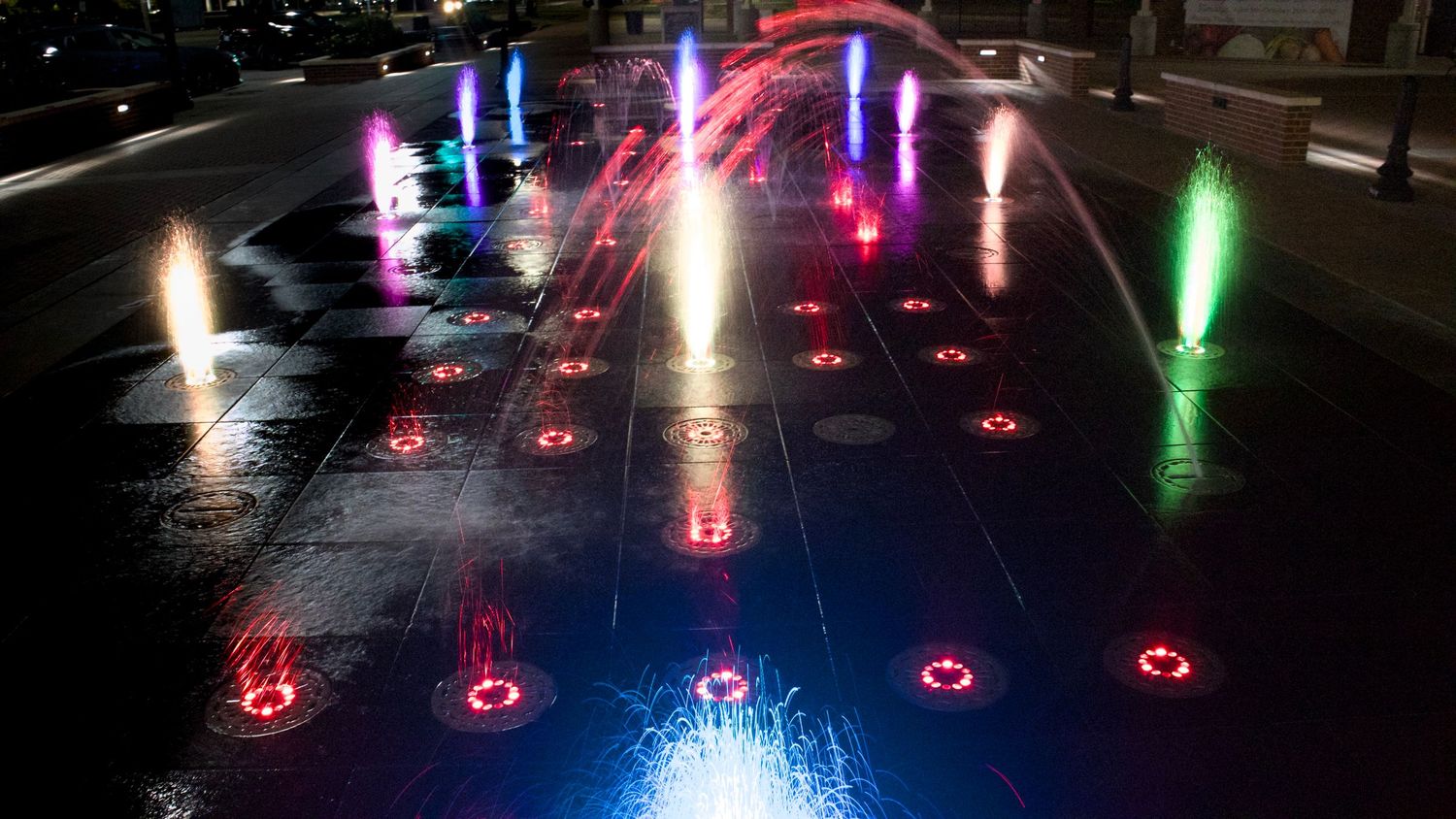 Nighttime long-exposure photography of a colorful illuminated water fountain at a public plaza, by Haug & Bees Media.