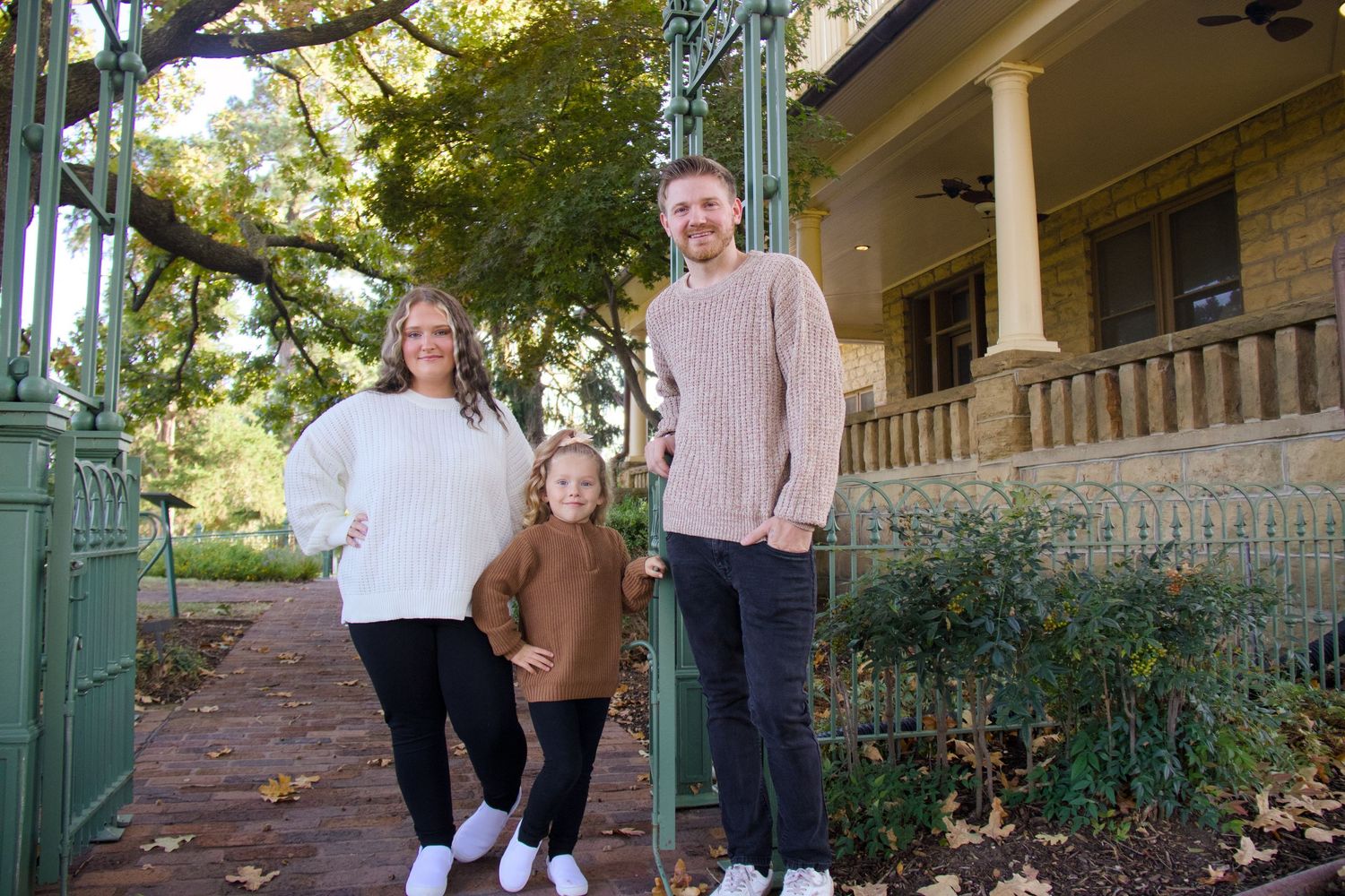 Full-length family lifestyle portrait by Haug & Bees Media, featuring a family in autumn attire standing before a historic stone estate with