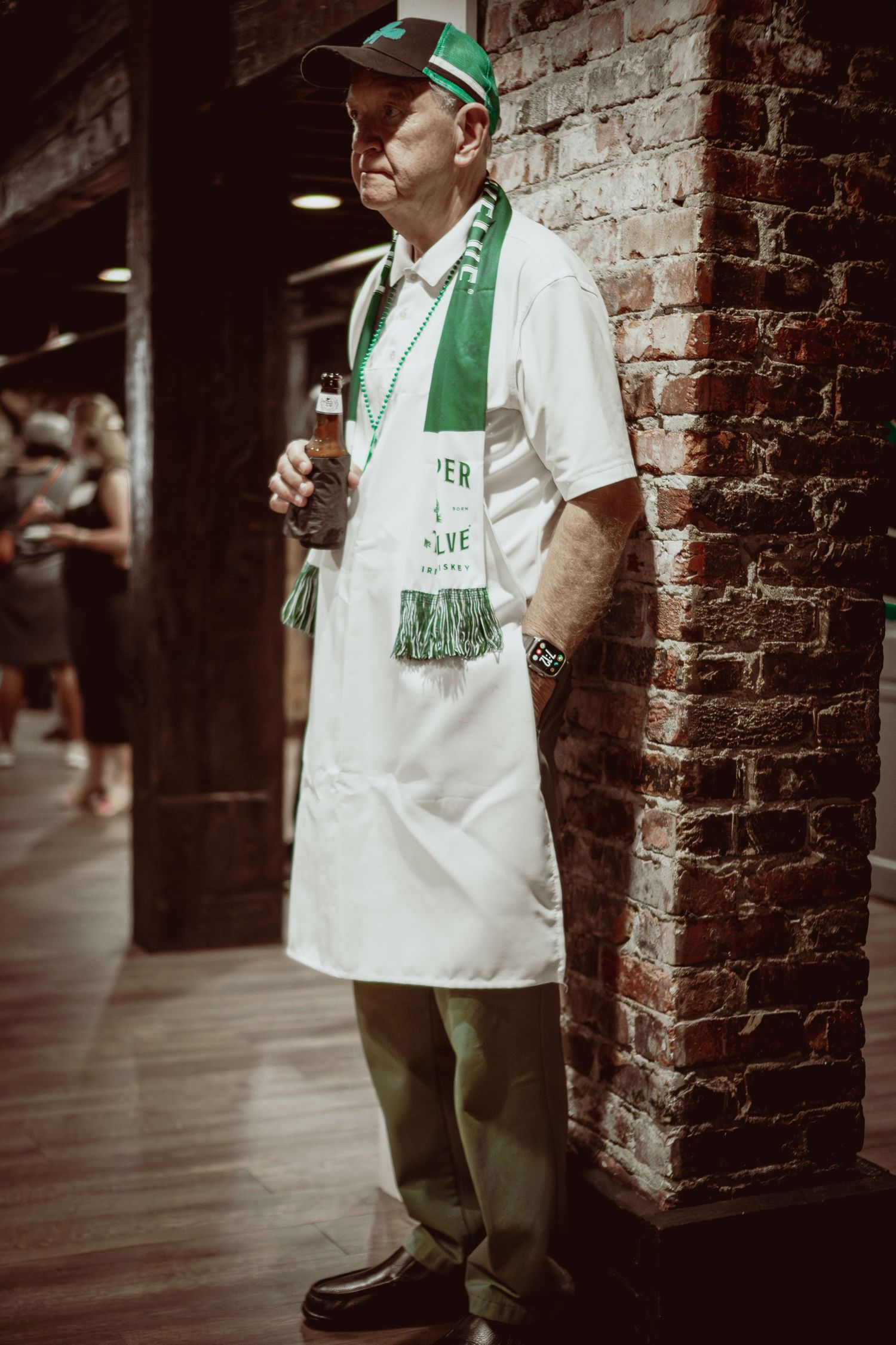 Person wearing green and white sports attire standing against brick wall.