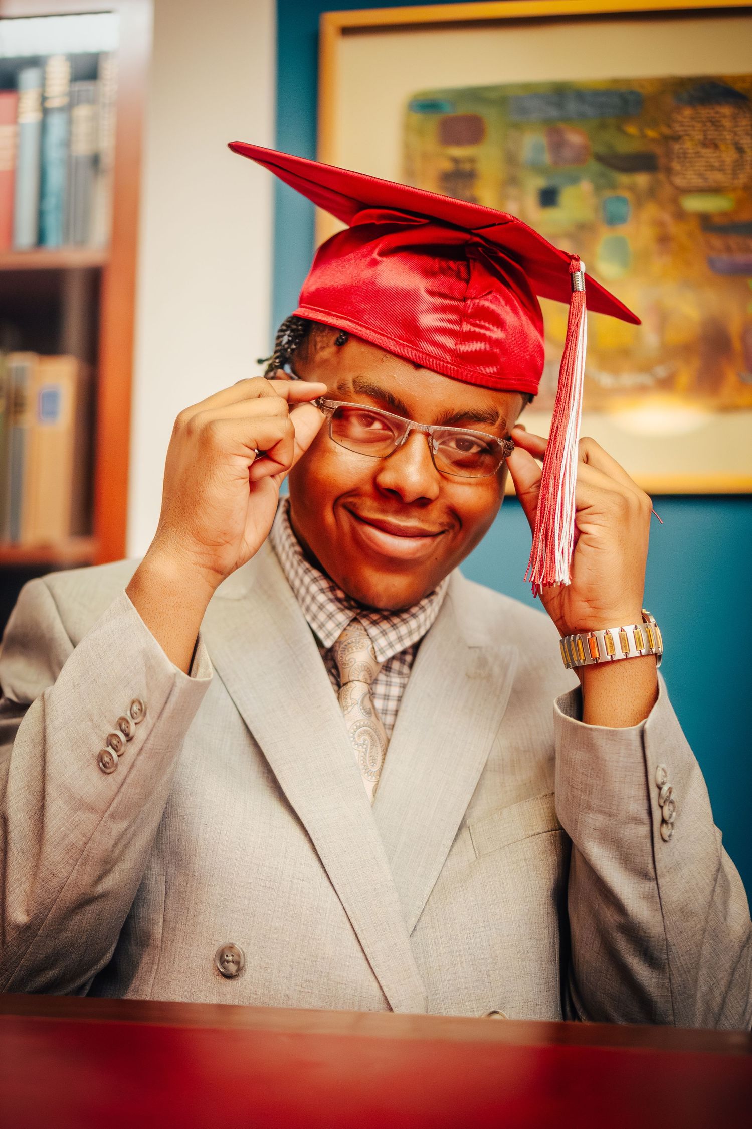 Graduate in light gray suit and red cap posing with playful gestures.