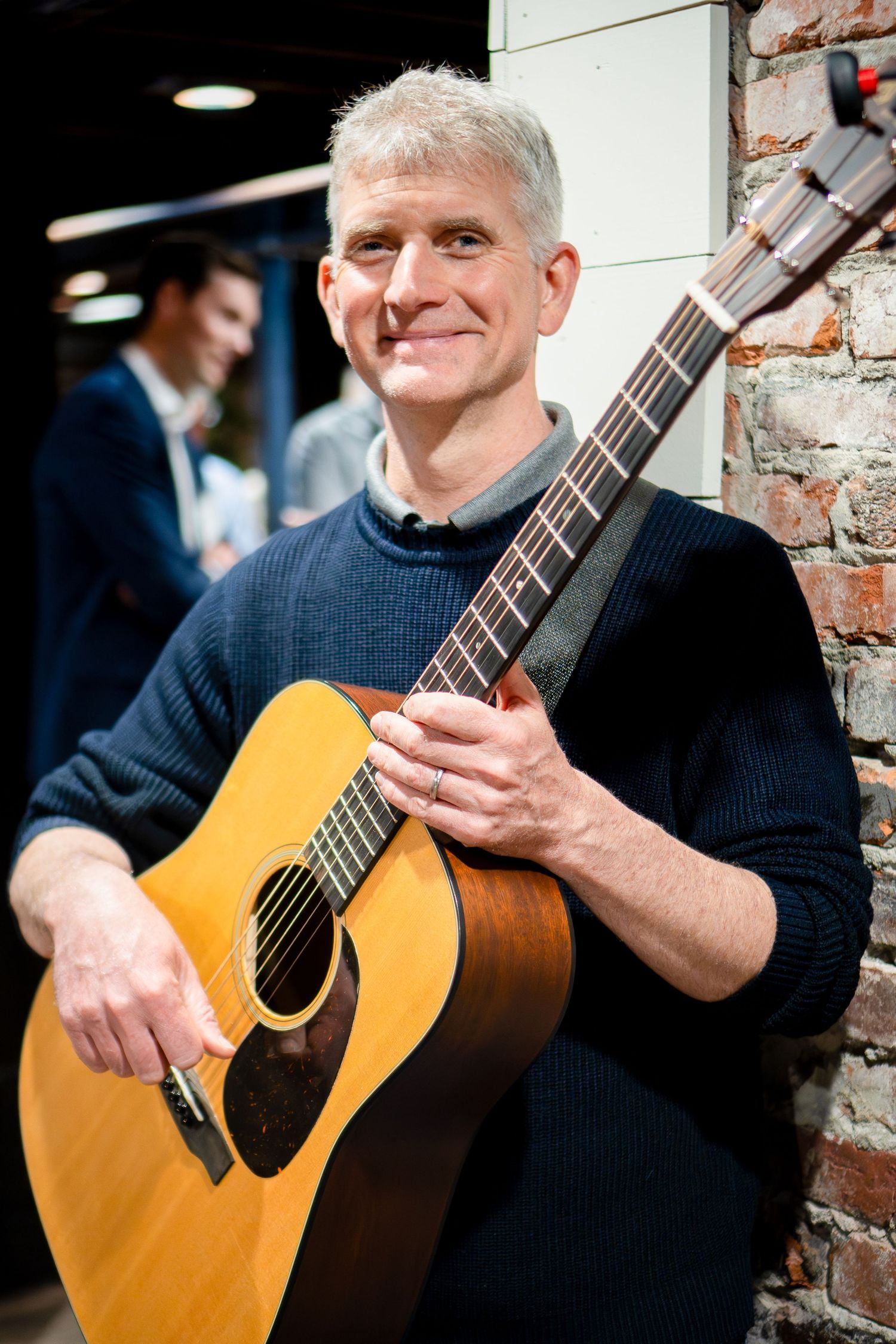 Musician playing acoustic guitar against exposed brick wall background.