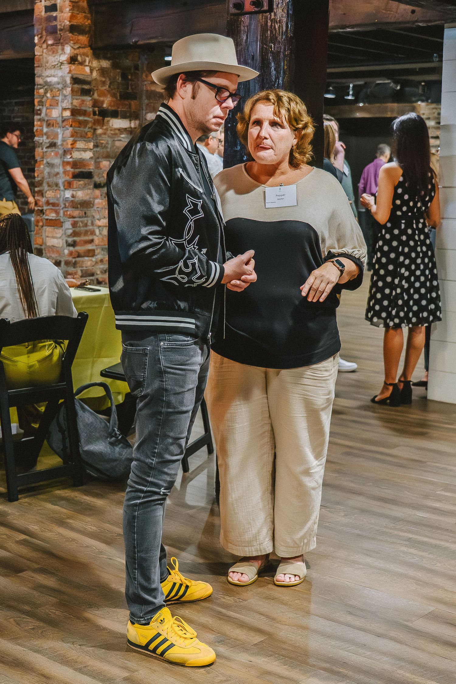 People mingling in casual attire on a wooden floor with exposed brick walls.