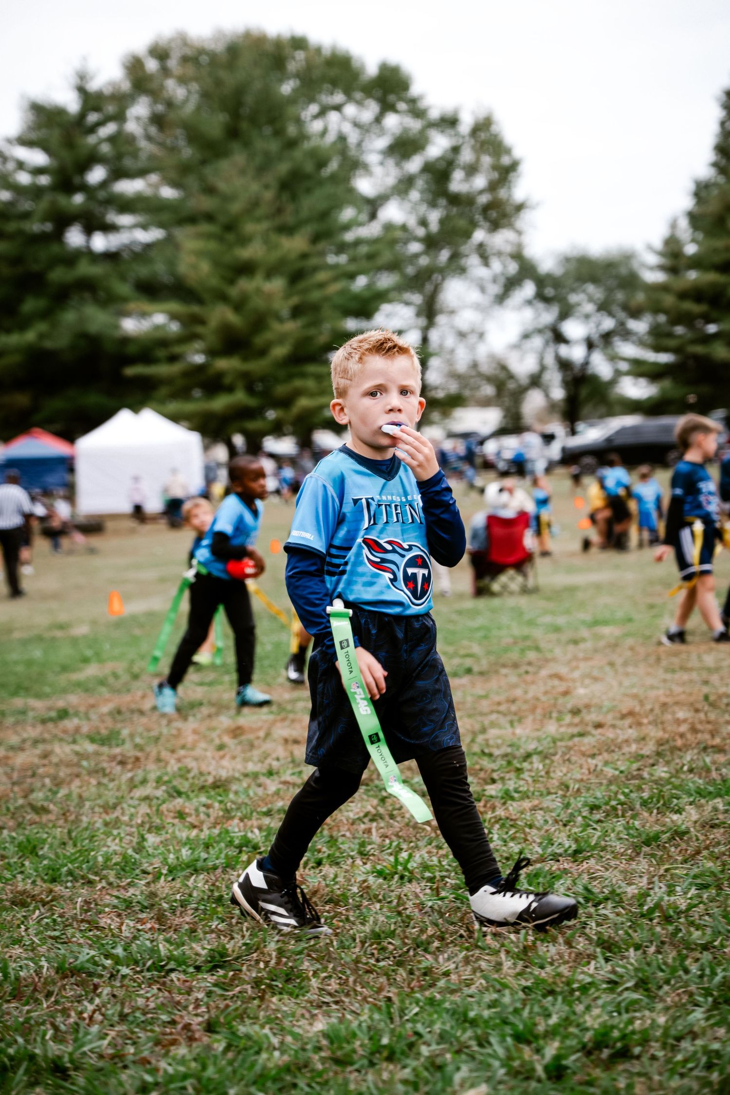 Child in blue Titans jersey running and playing in grassy outdoor area.