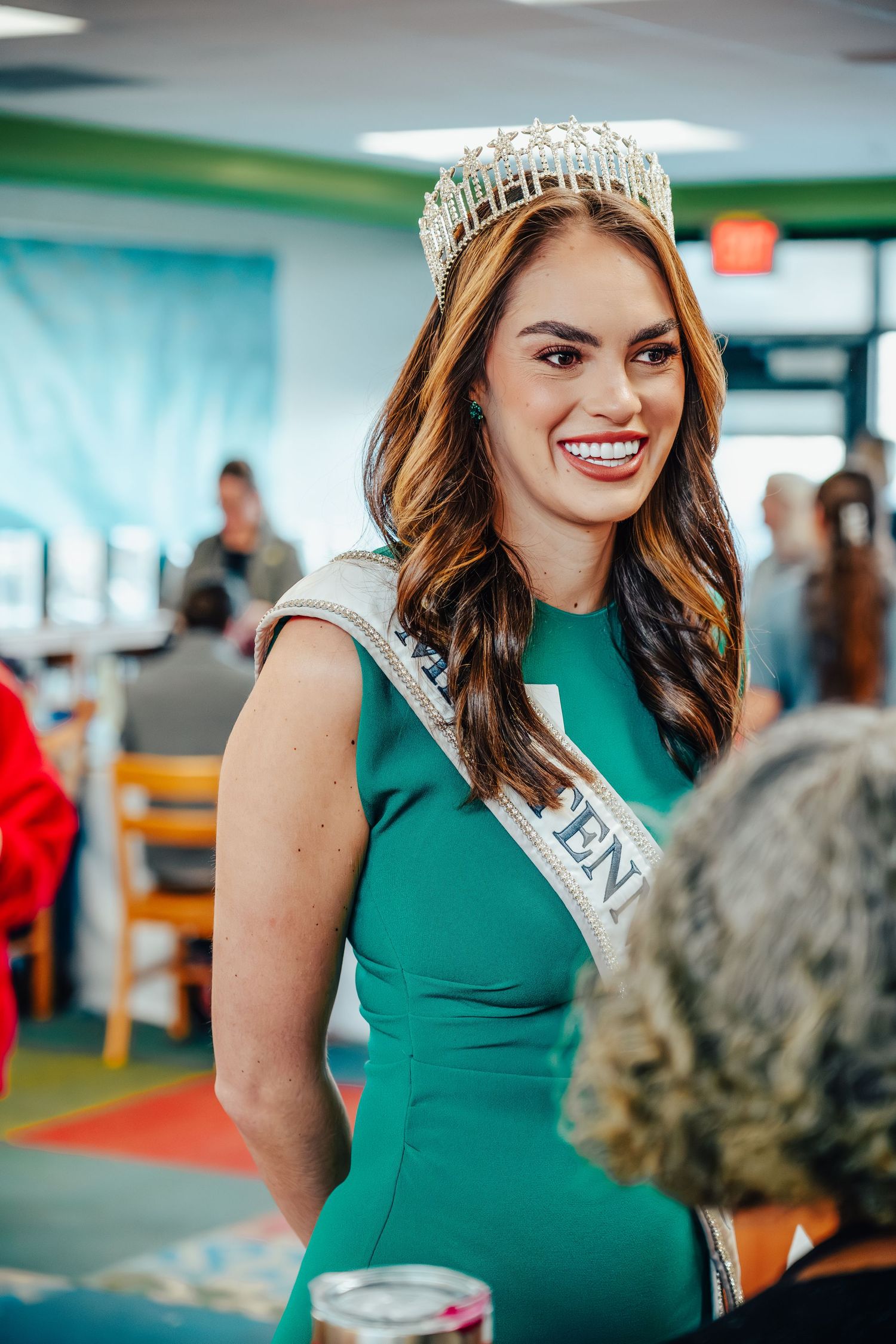 Woman in emerald green dress wearing a crown at a military event.