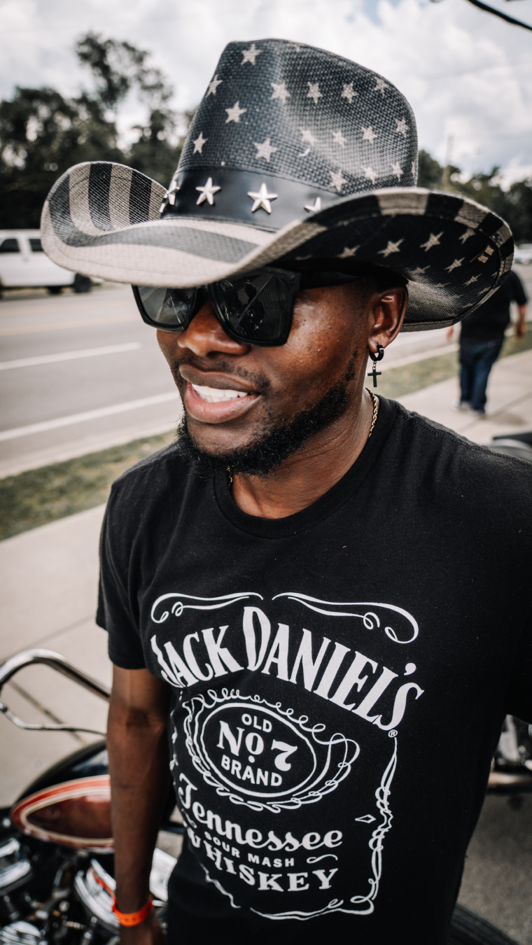 Person wearing Jack Daniel's t-shirt and American flag cowboy hat outdoors.