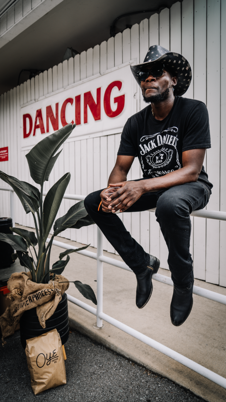 Person in black clothing sitting with Oye coffee bag near a wall with Dancing text.