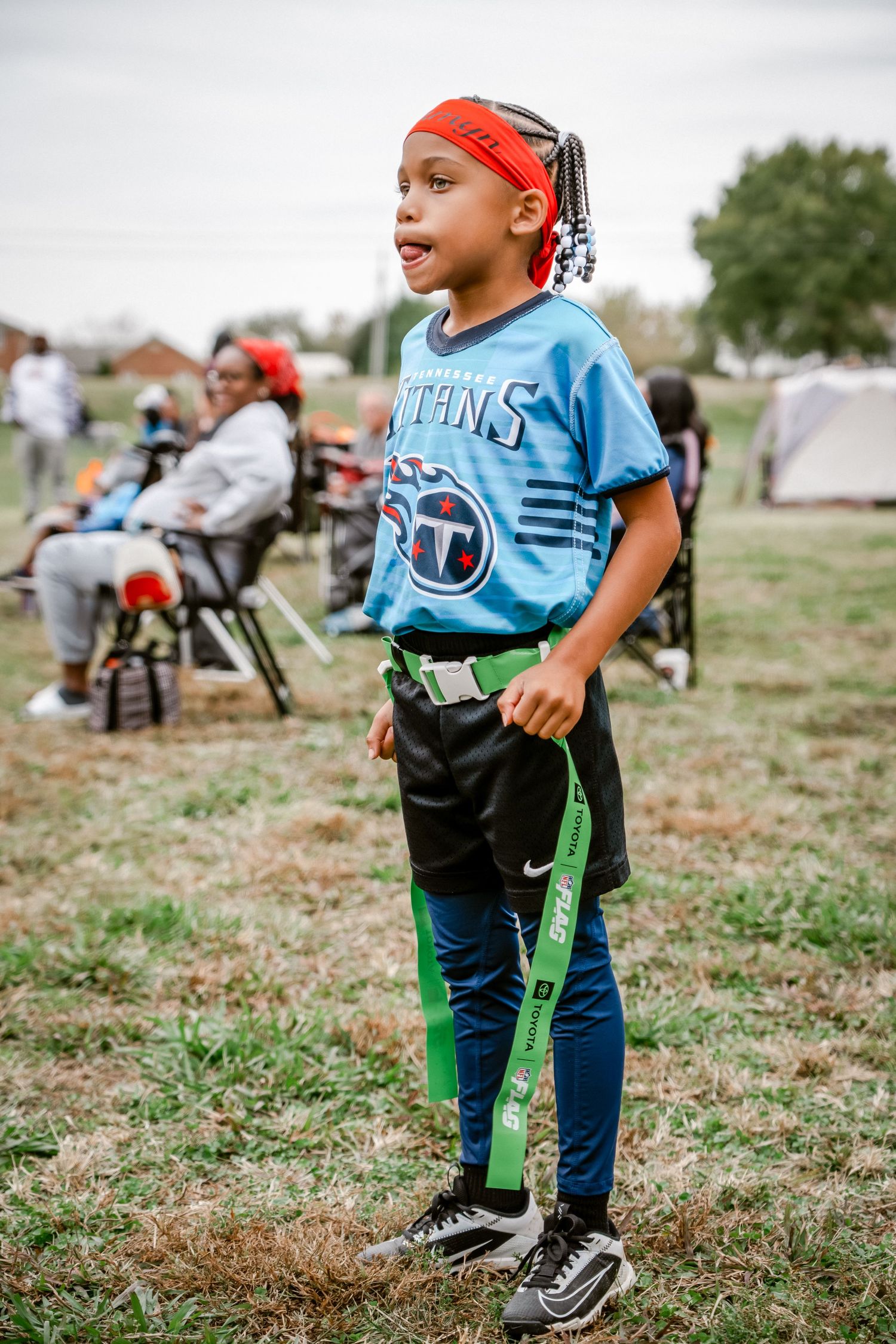 Child wearing Titans jersey and jeans playing in a field with tents in background.