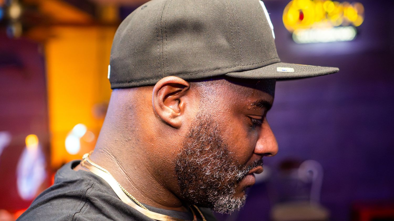 Profile view of person in baseball cap against warm-lit background.