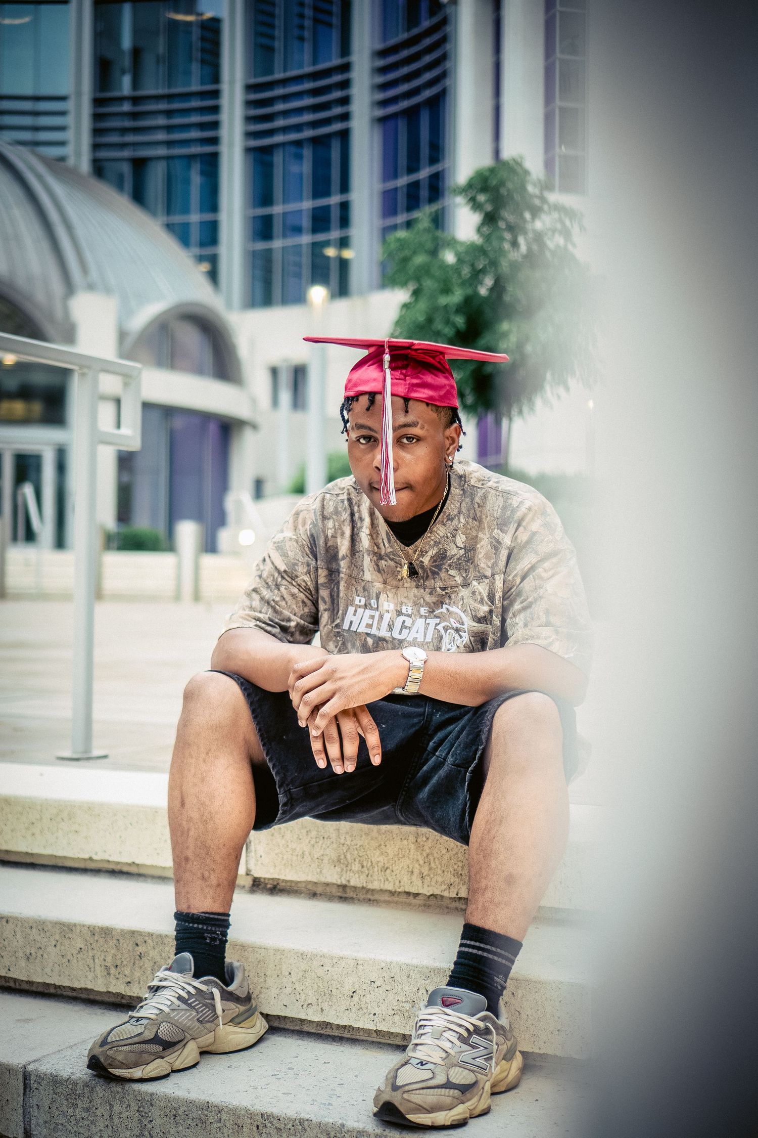 Person in red cap sitting on concrete ledge outside modern building.