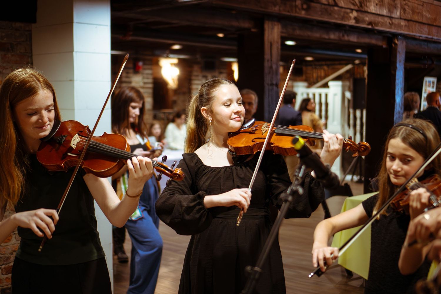 Musicians performing with violins in dimly lit indoor venue.