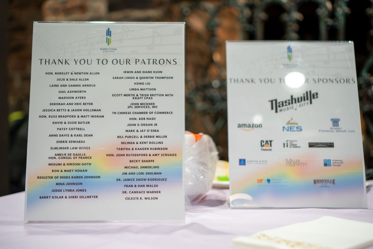 A row of patron acknowledgment signs with rainbow prism effects displayed on white surfaces.