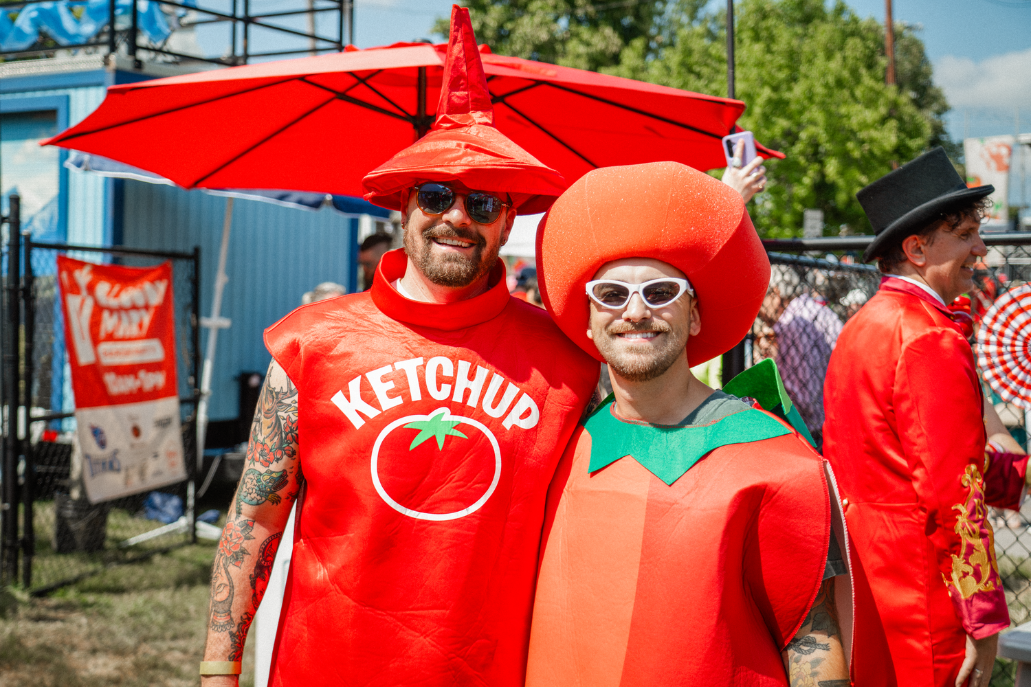 Festive crowd wearing bright red shirts gathered outdoors under a tent at a summer event.