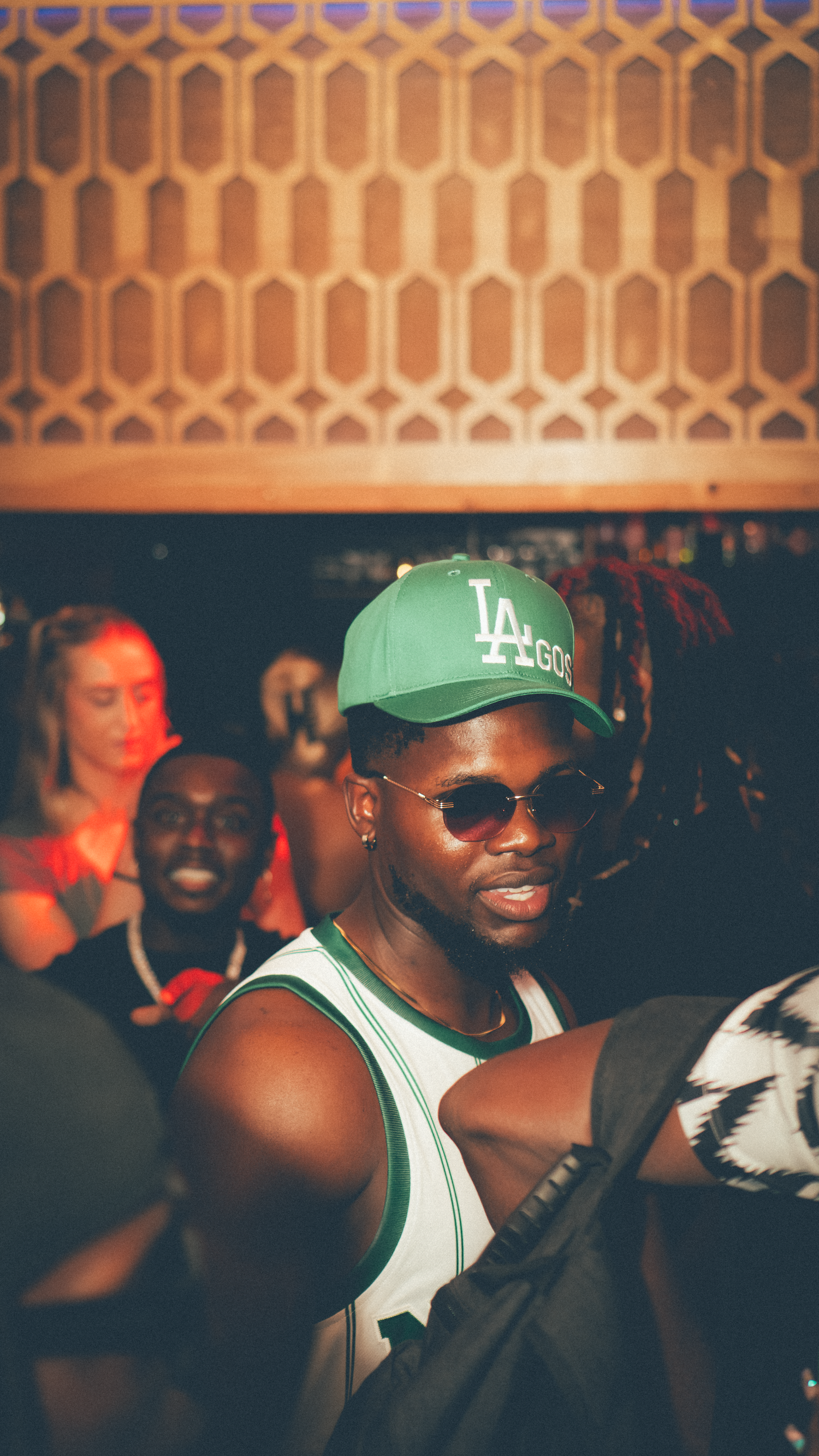 People enjoying a lively event with LA sports gear and sunglasses in a dimly lit venue.