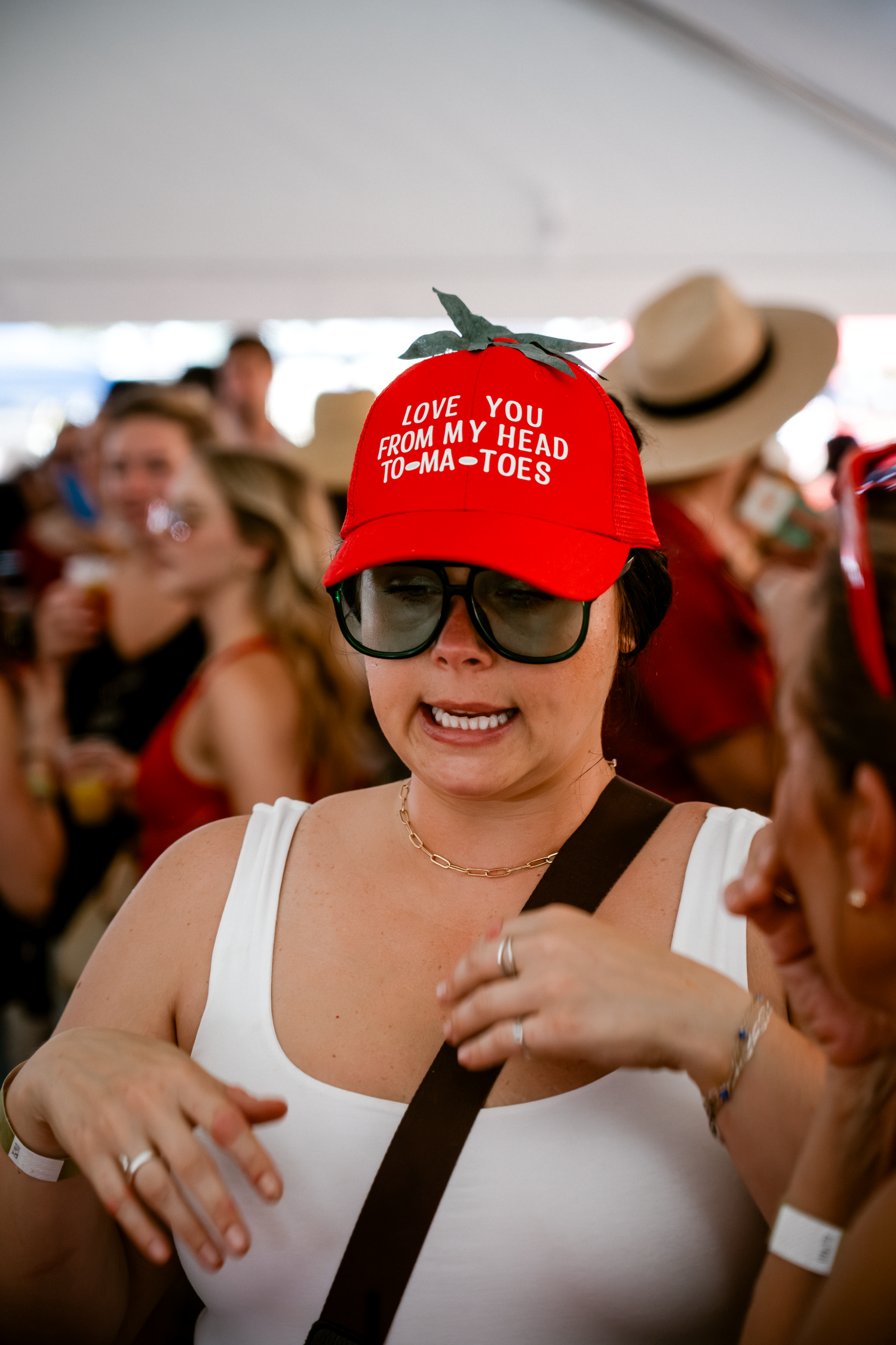 Festival-goers wearing red baseball caps with fun slogans at an outdoor event.