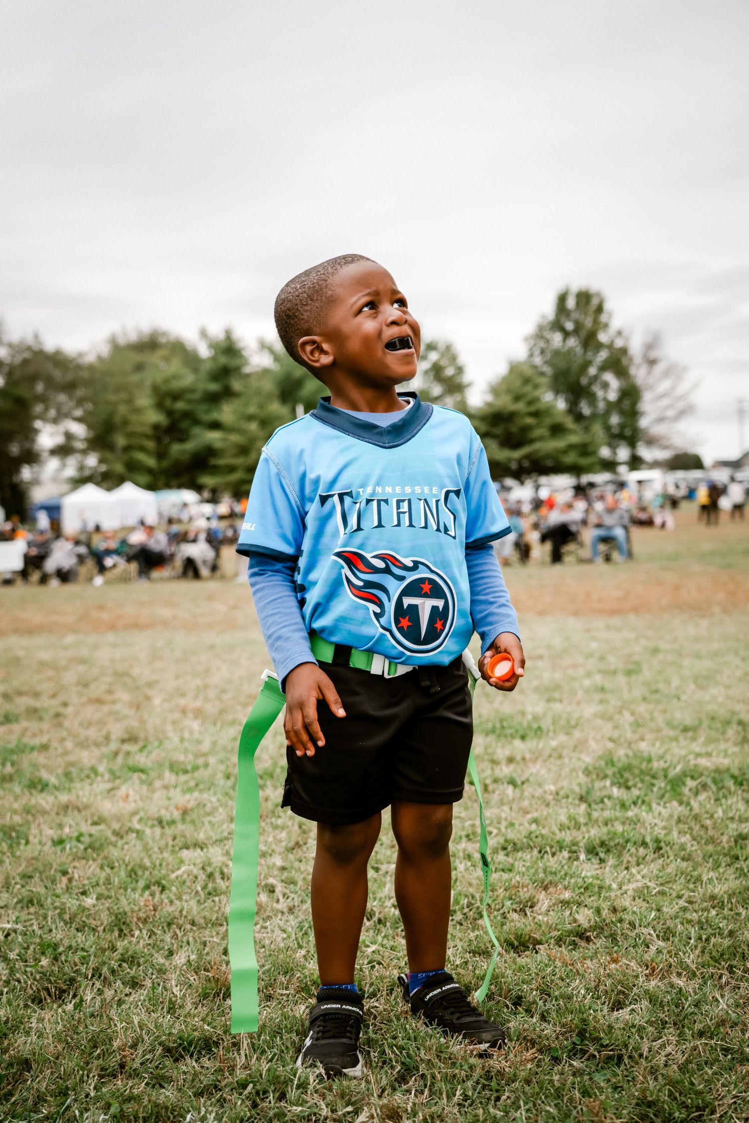 Young child in Tennessee Titans jersey playing outdoors on grassy field.