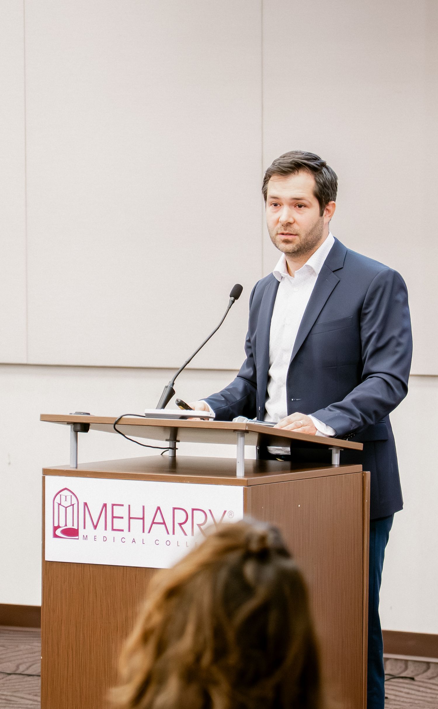 Speaker at podium presenting at Mehardy Medical conference in professional attire.