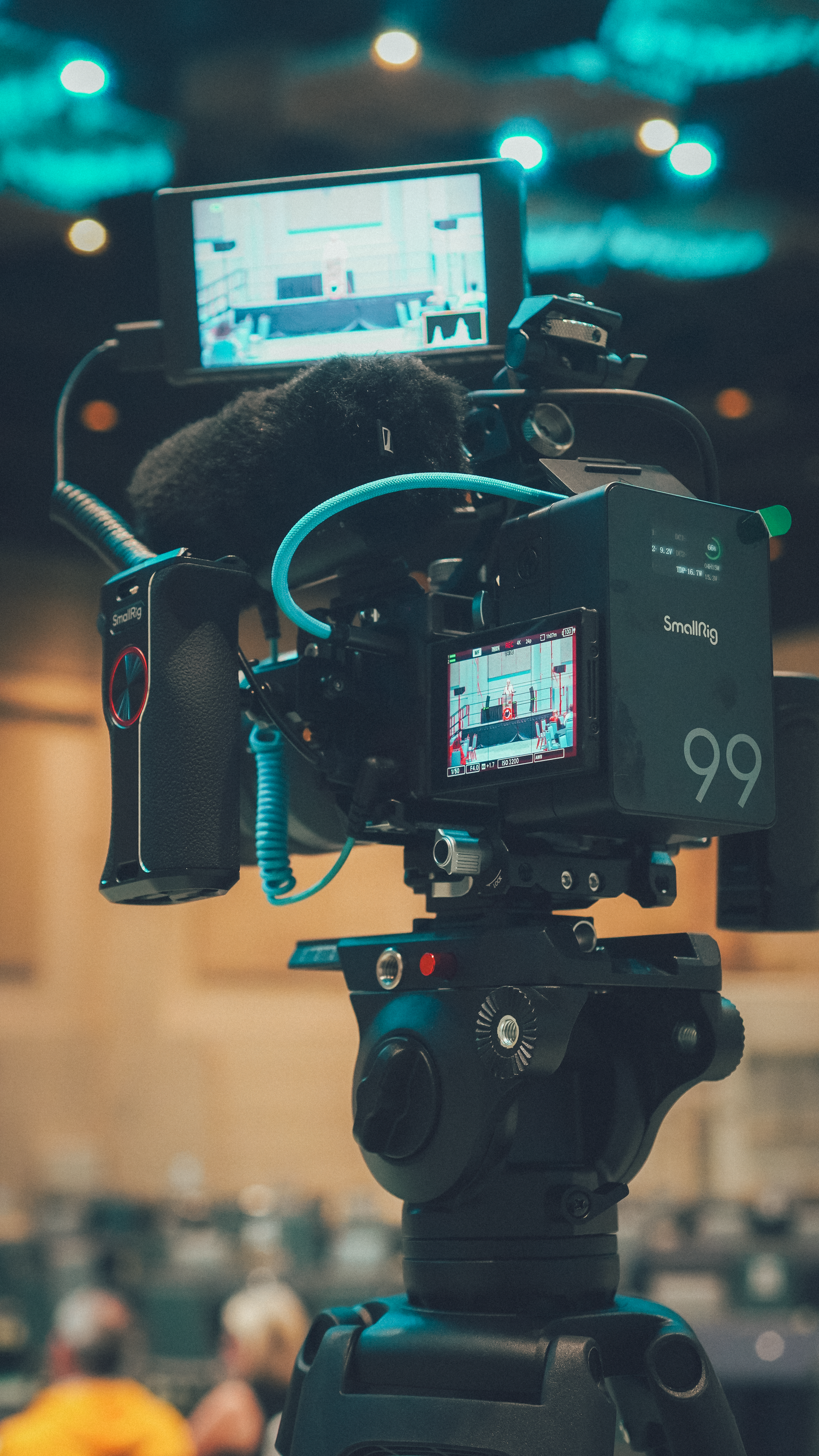 Professional video cameras set up on tripods with turquoise lighting in background.