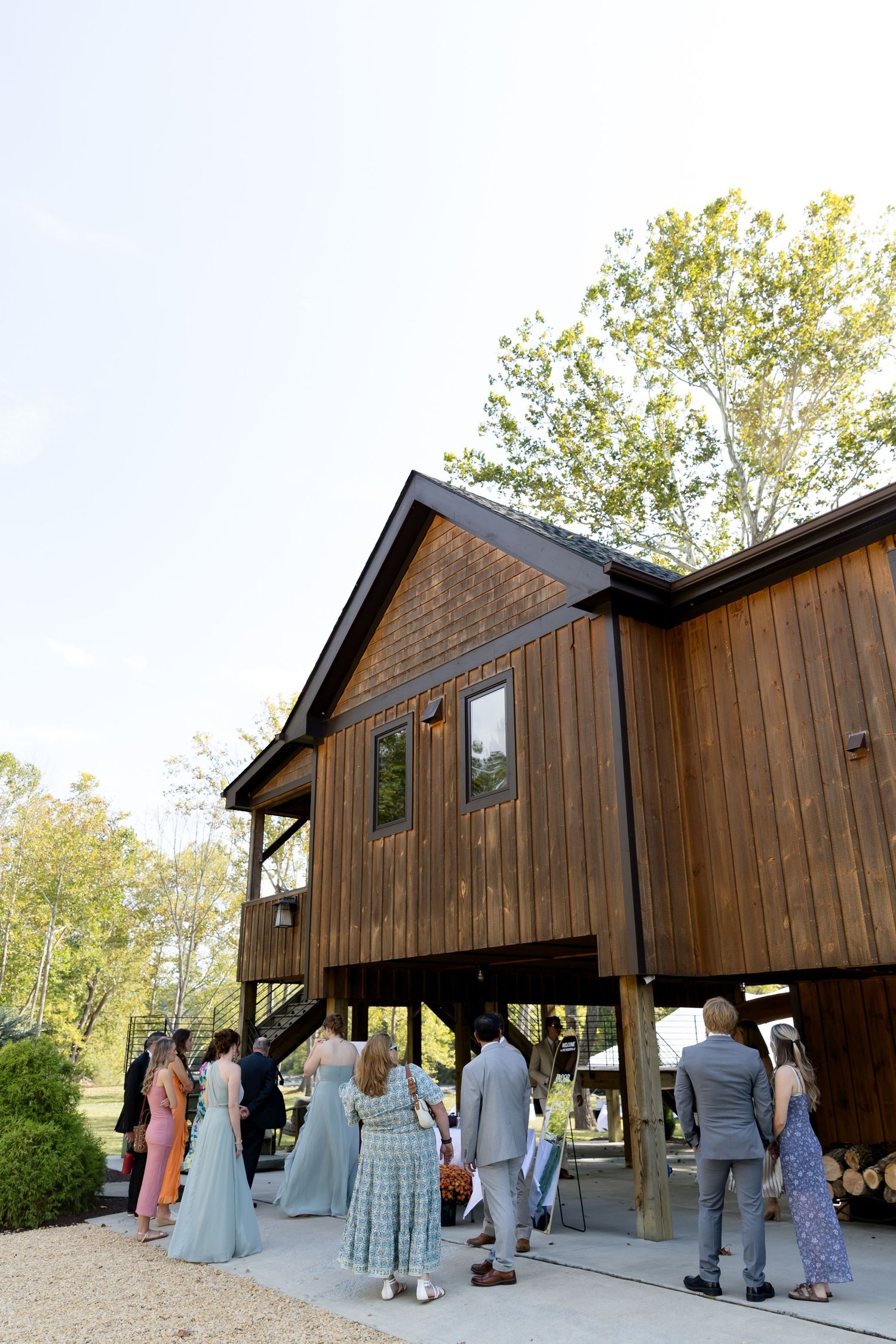 Wedding guests gathering outside a rustic elevated wooden barn venue on a sunny day.
