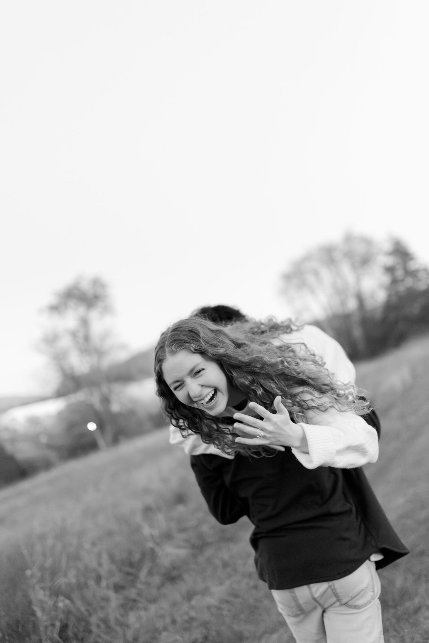 Black and white photo of a joyful woman laughing while being embraced by her partner in an open field.